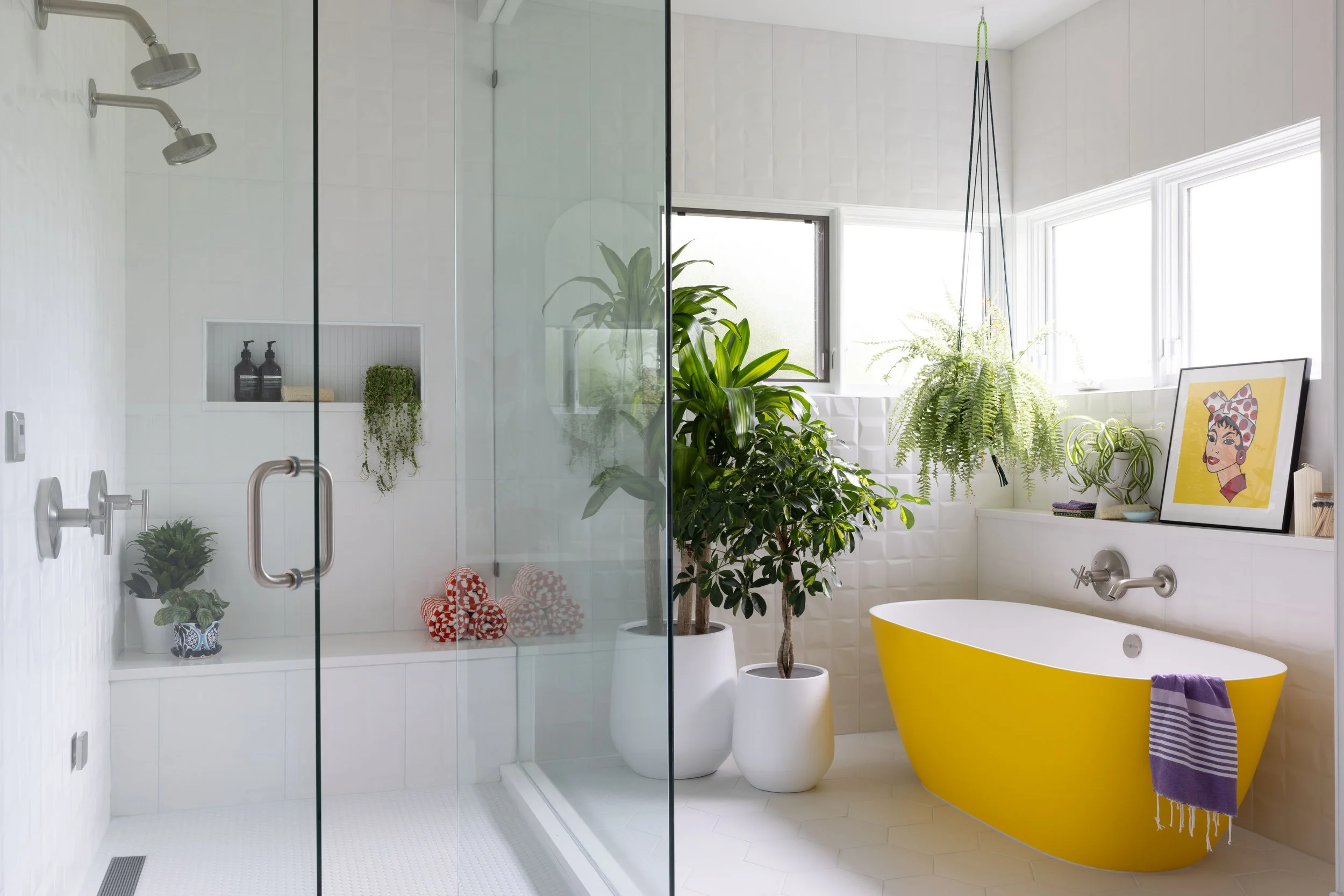 Durango bathroom with a yellow freestanding tub, glass shower, white tile, silver fixtures, and hanging plants.