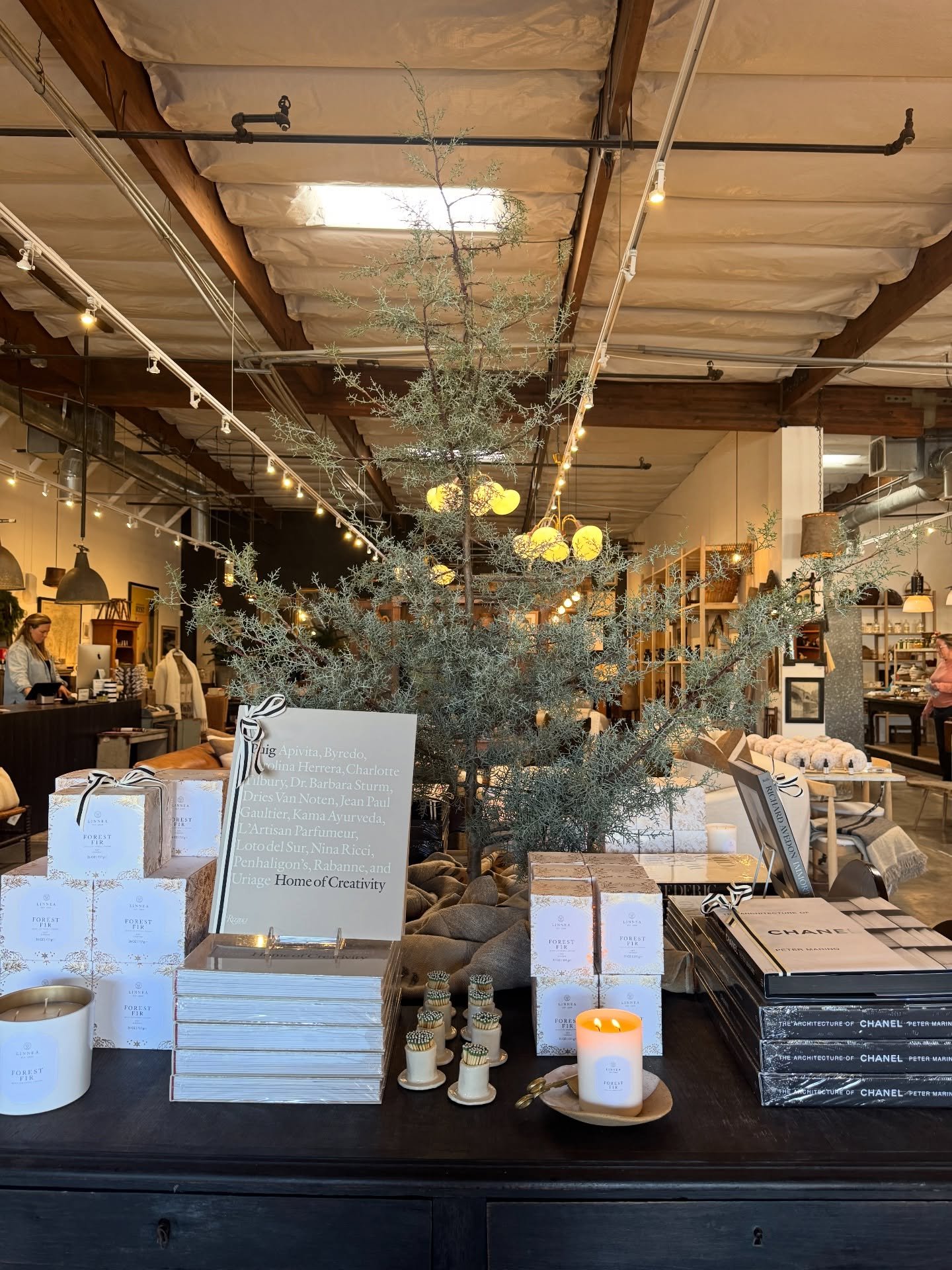 Shop display of books, bowls, branches, and decorative objects beneath timber beams.