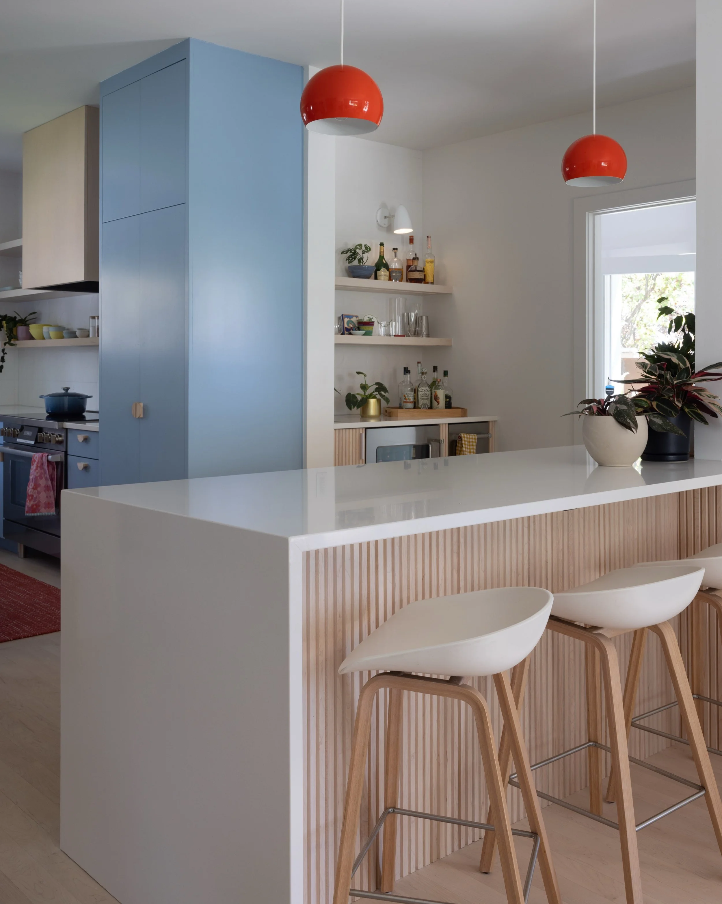 Kitchen island with a pale counter, wood stools, blue cabinetry, and red pendant lights.