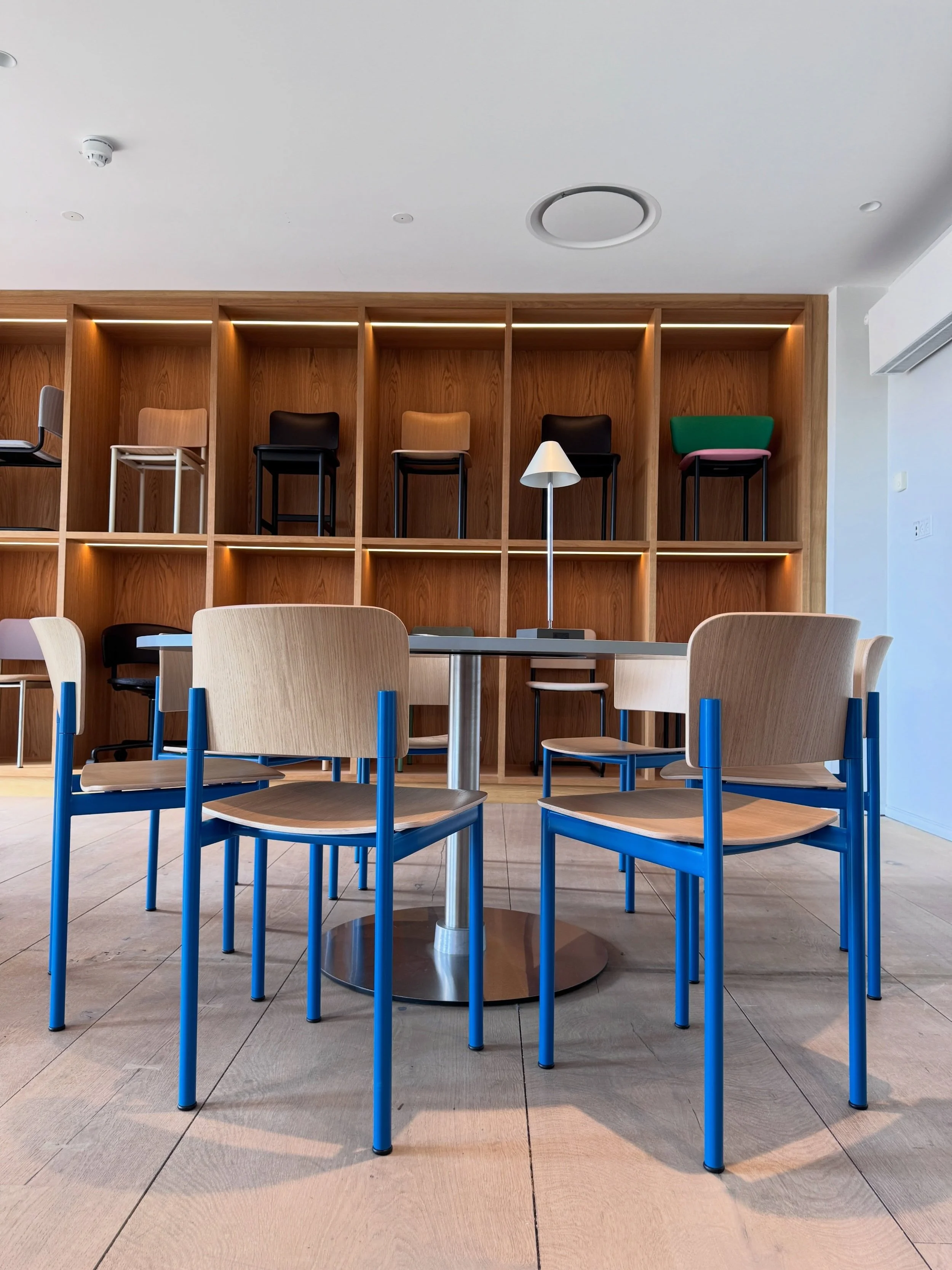 Copenhagen furniture showroom with blue-framed chairs, oak tables, shelving, and warm wood paneling.