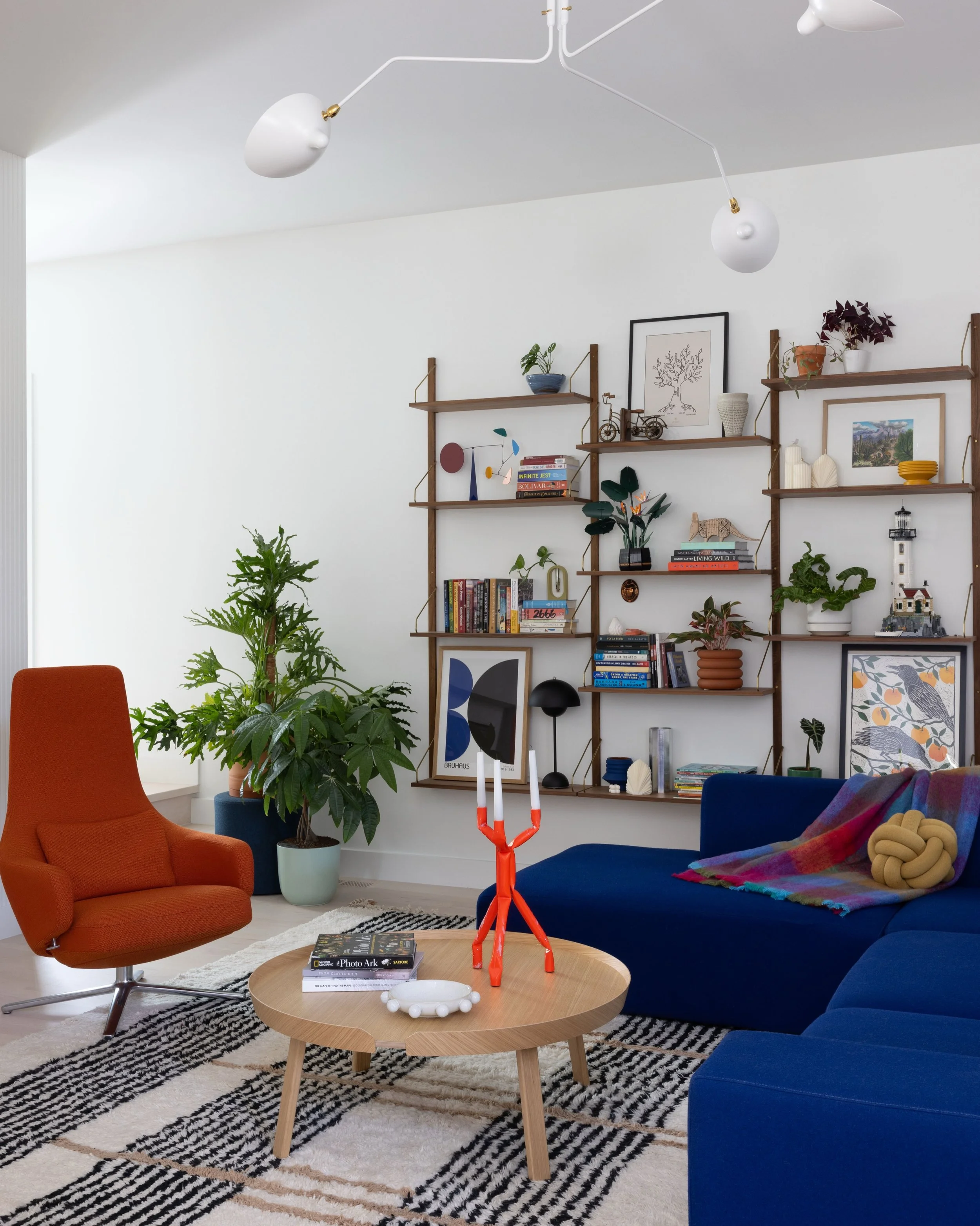 Living room with a blue sofa, orange lounge chair, patterned rug, and open wood shelves.