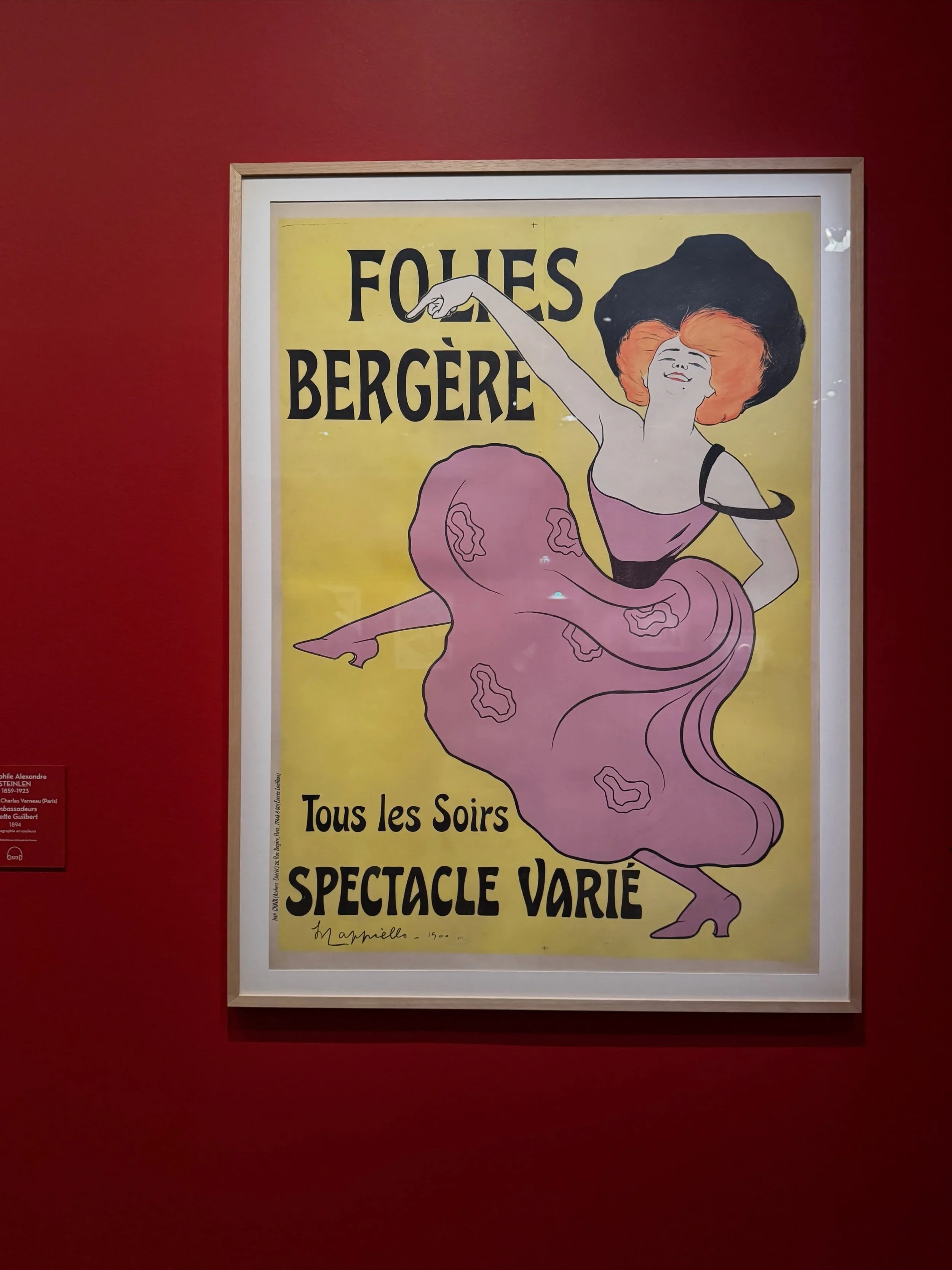 Framed Folies Bergère poster against a red museum wall in Paris.