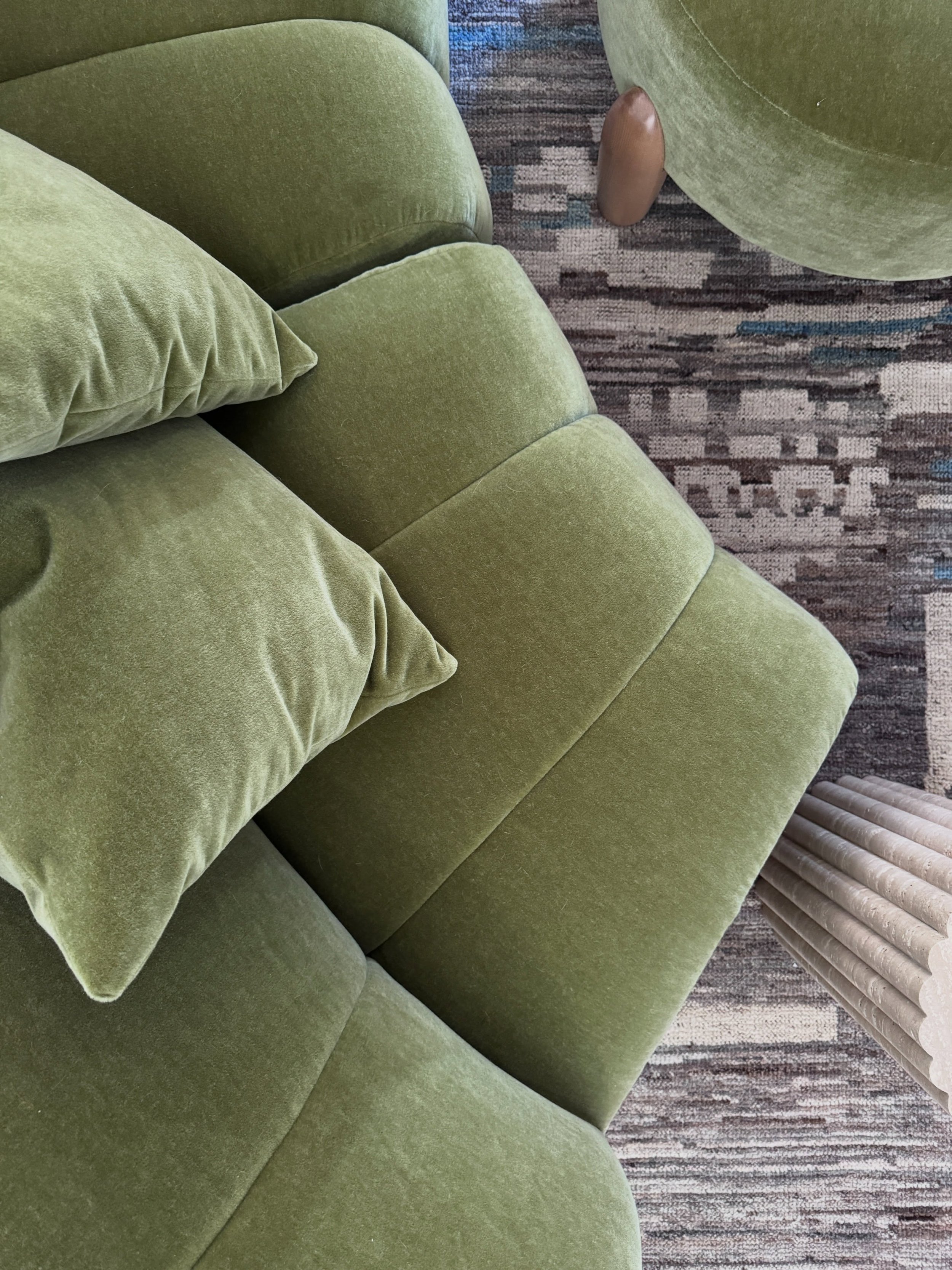 Olive green mohair upholstery with deep horizontal channels beside a patterned rug.