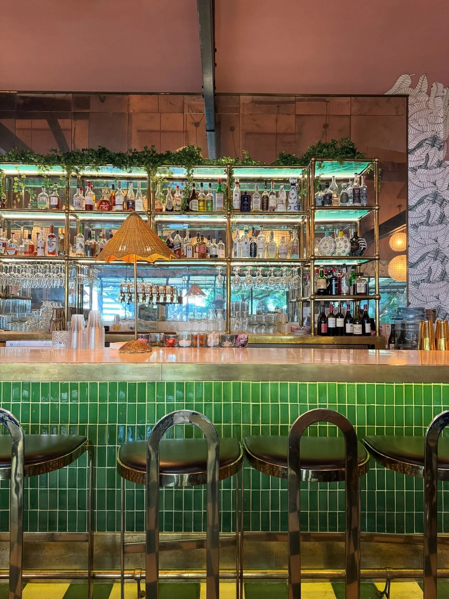 Green-tiled Palm Springs bar with brass details, stools, and backlit bottle shelves.