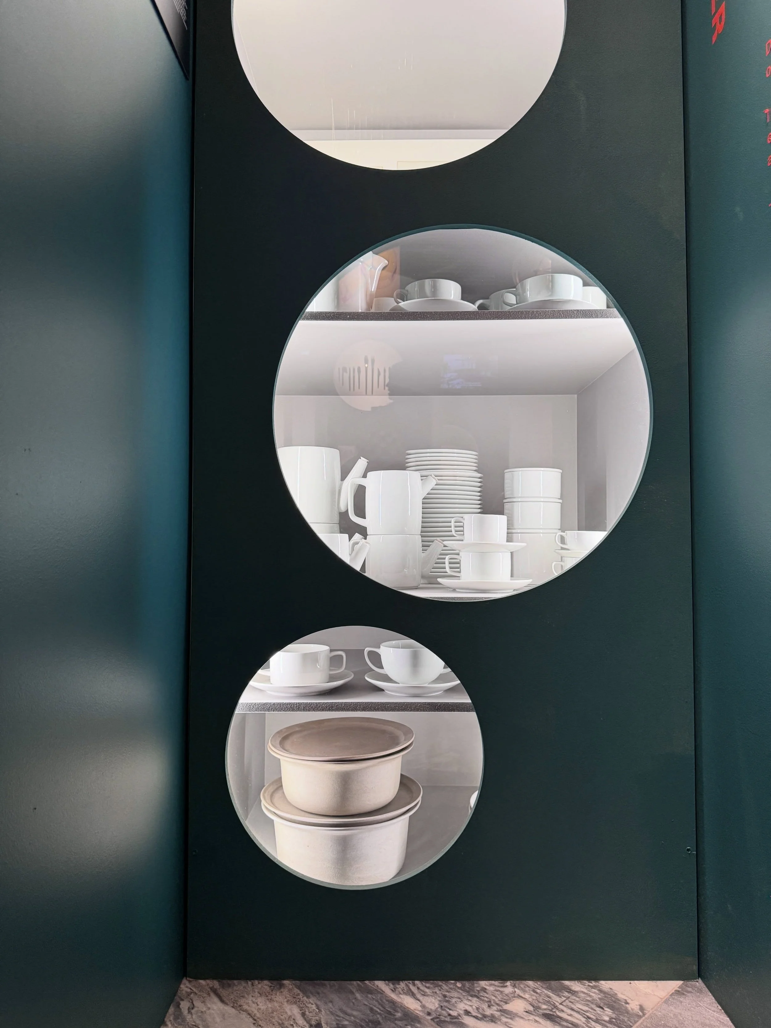 Dark green museum display with circular openings showing white ceramics and tableware.