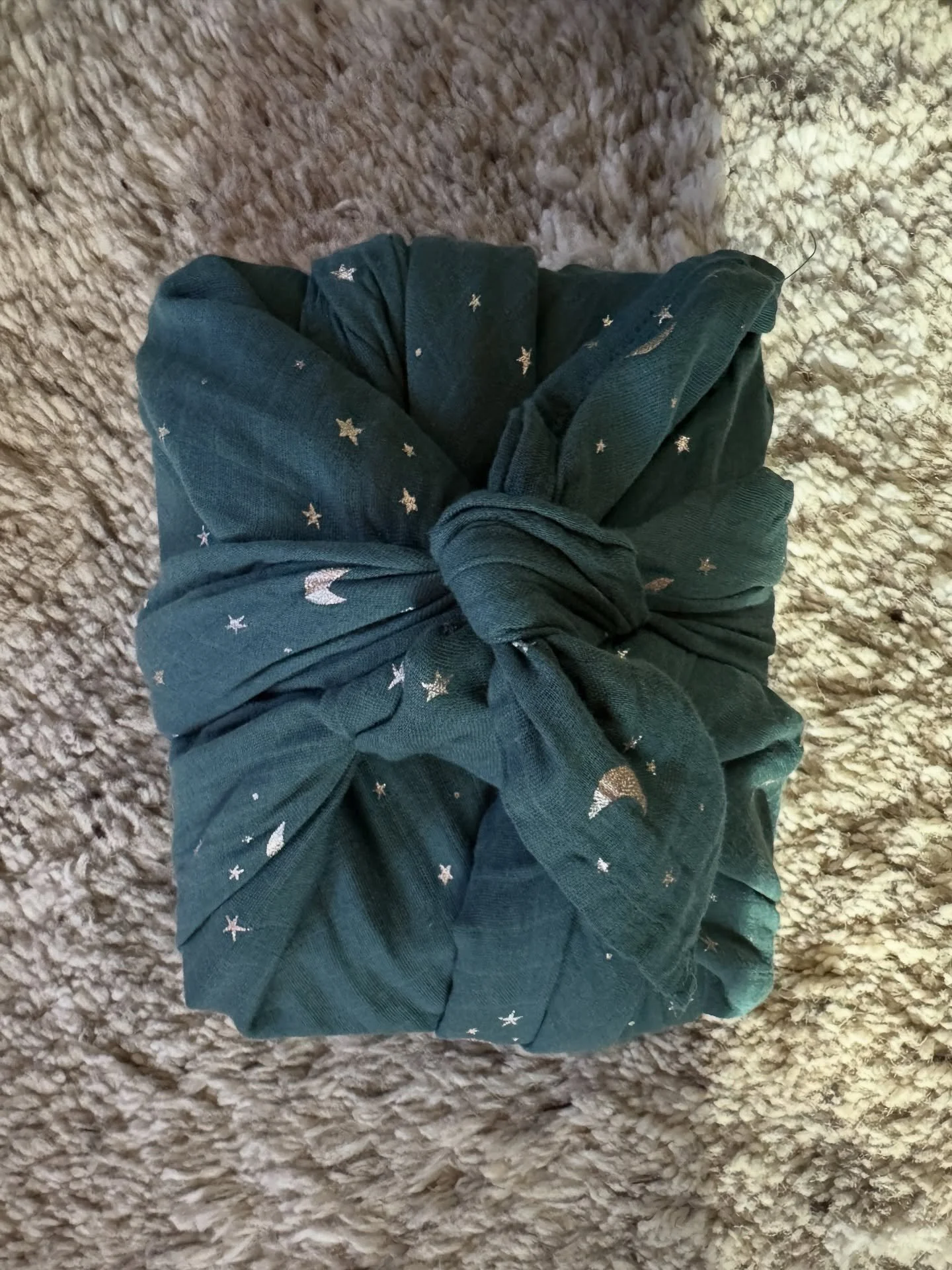 Gift wrapped in dark green patterned fabric and tied with a fabric knot.