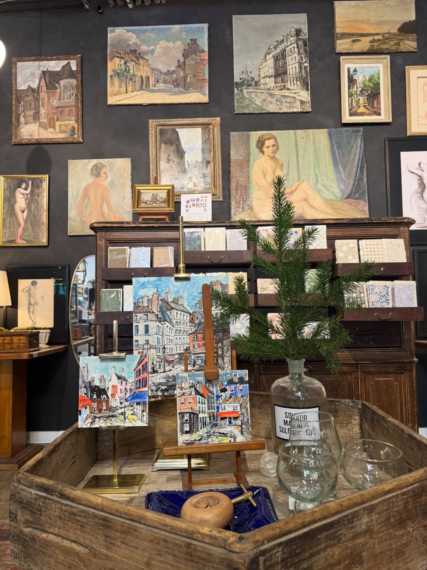 Vintage shop wall with framed paintings above a wood table and decorative objects.