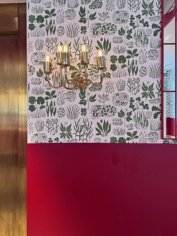 Green botanical wallpaper above burgundy wall paneling with a brass chandelier at Svenskt Tenn.