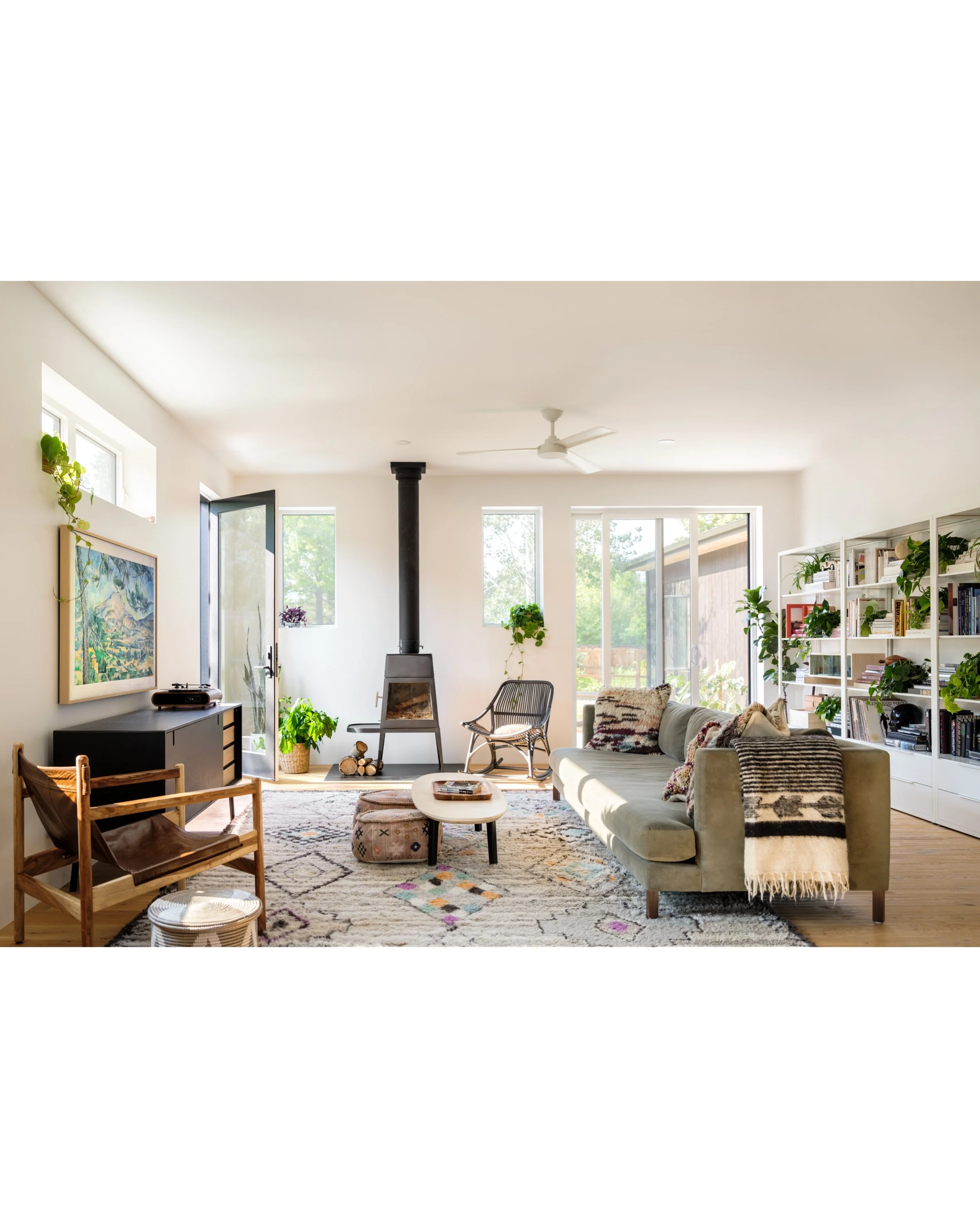 Living room with pale seating, a black stove, wood floors, patterned rugs, and large windows.
