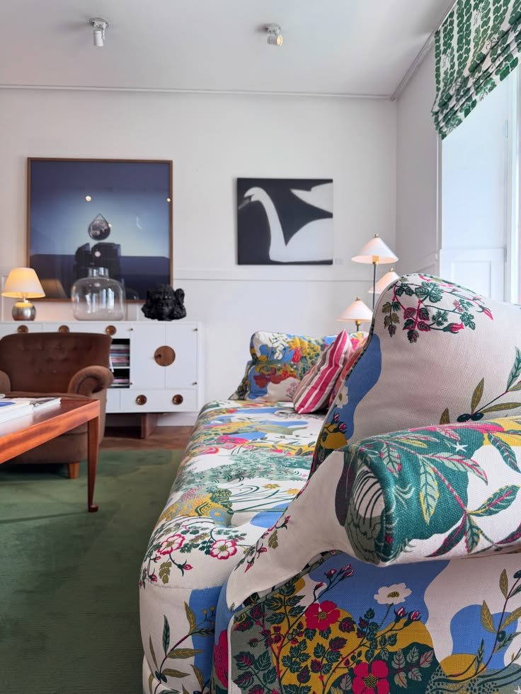 Floral upholstered sofa with patterned cushions, framed art, and green carpet at Svenskt Tenn.