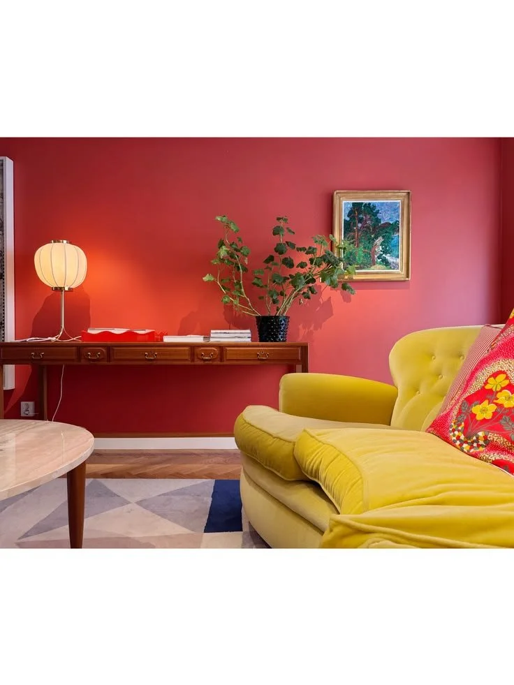 Yellow upholstered armchair with a floral cushion in a red room with a low cabinet and white globe lamp at Svenskt Tenn.