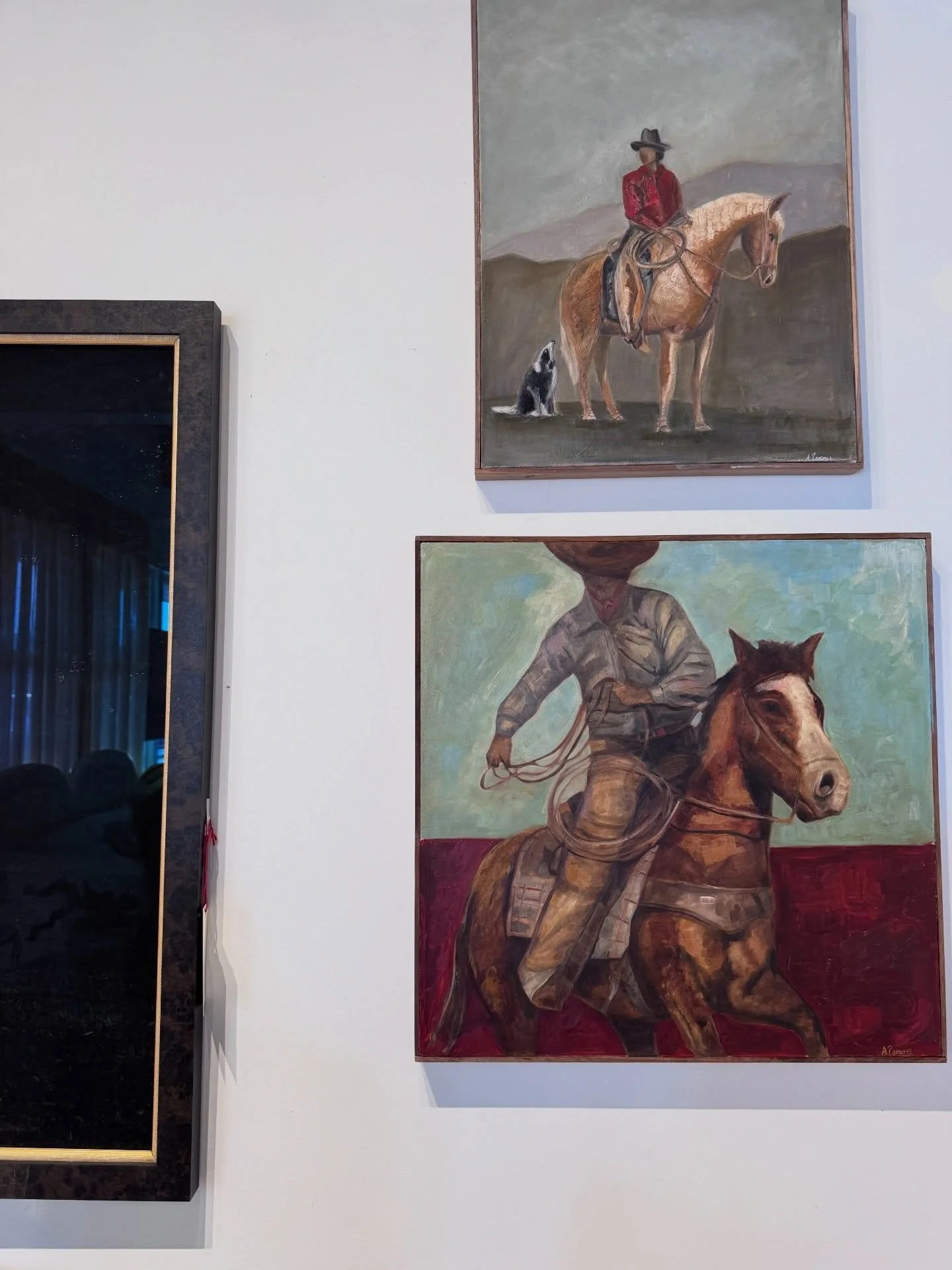 Framed horse-and-rider paintings displayed on a pale wall in a vintage shop.