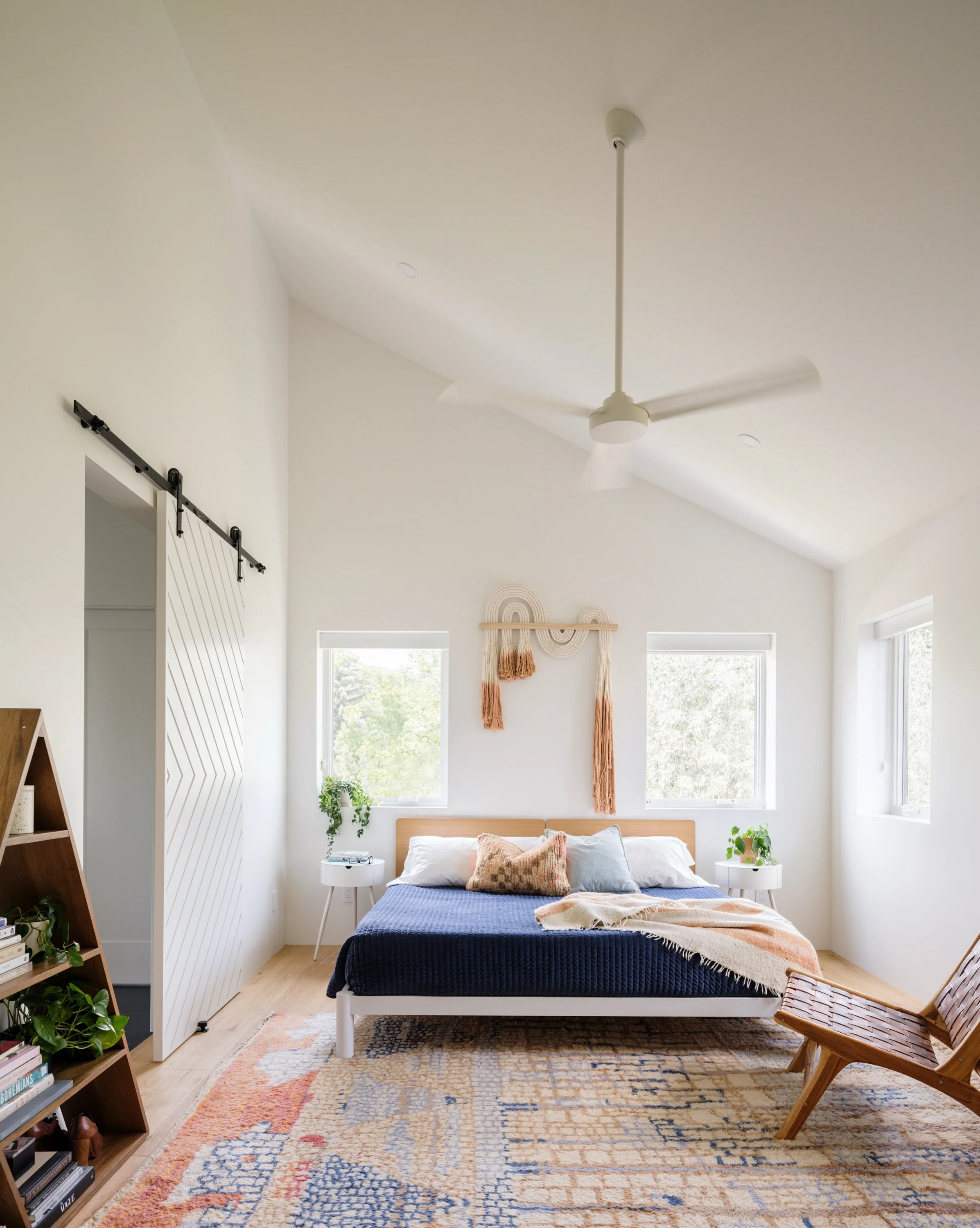 Bedroom with a pitched white ceiling, pale wood floor, upholstered bed, and layered rug.