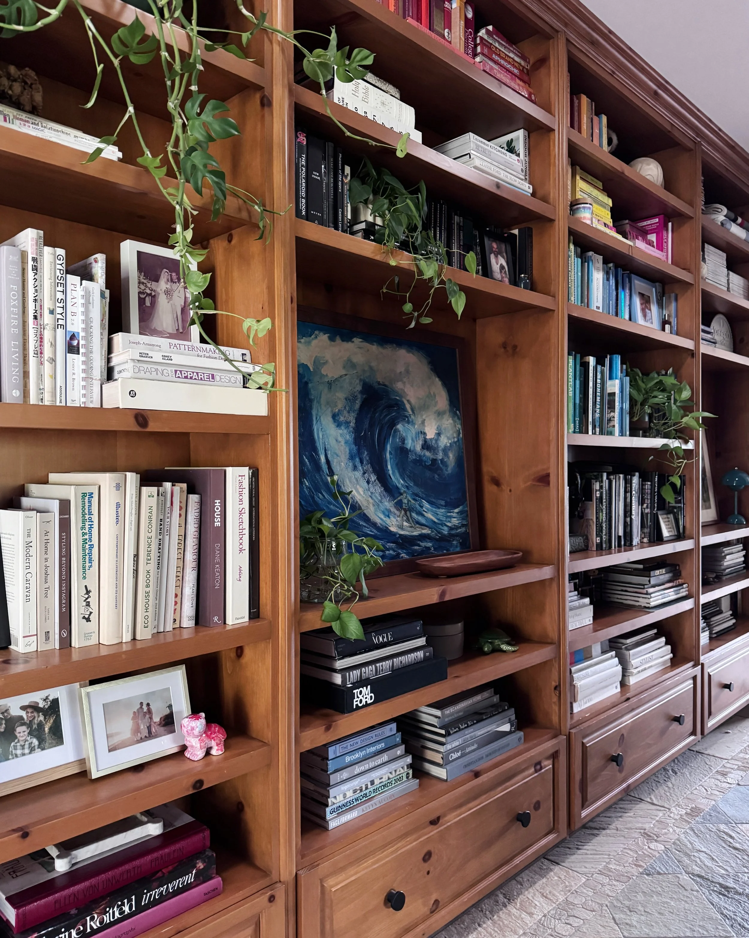 Wood bookshelves filled with books, framed art, ceramics, and trailing plants.