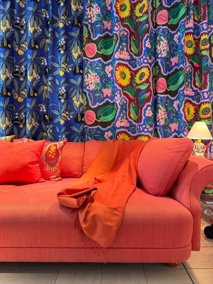 Orange sofa with red cushions beneath blue botanical curtains at Svenskt Tenn.
