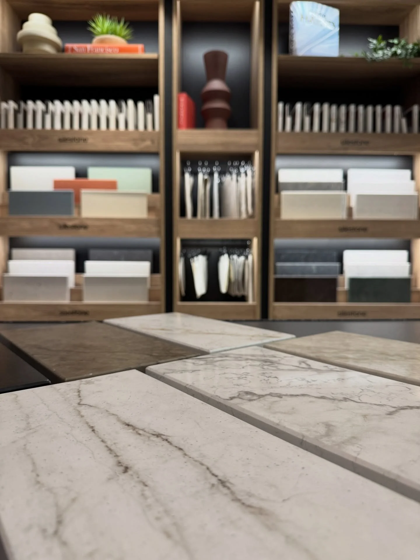 Material showroom with stone samples, tall display shelves, dark cabinetry, and a veined stone table.