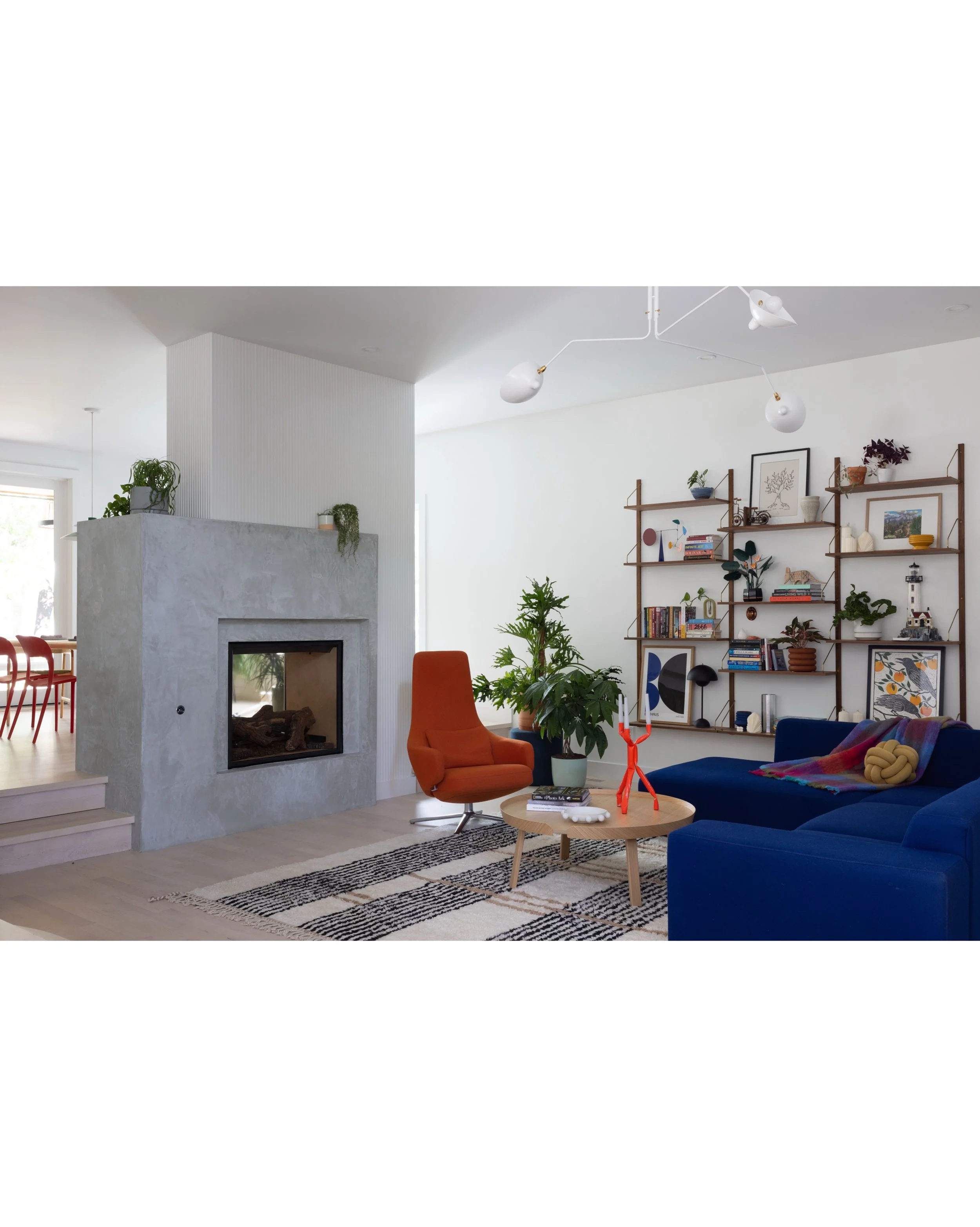 Open living room with blue seating, a concrete fireplace, layered rugs, and white walls.