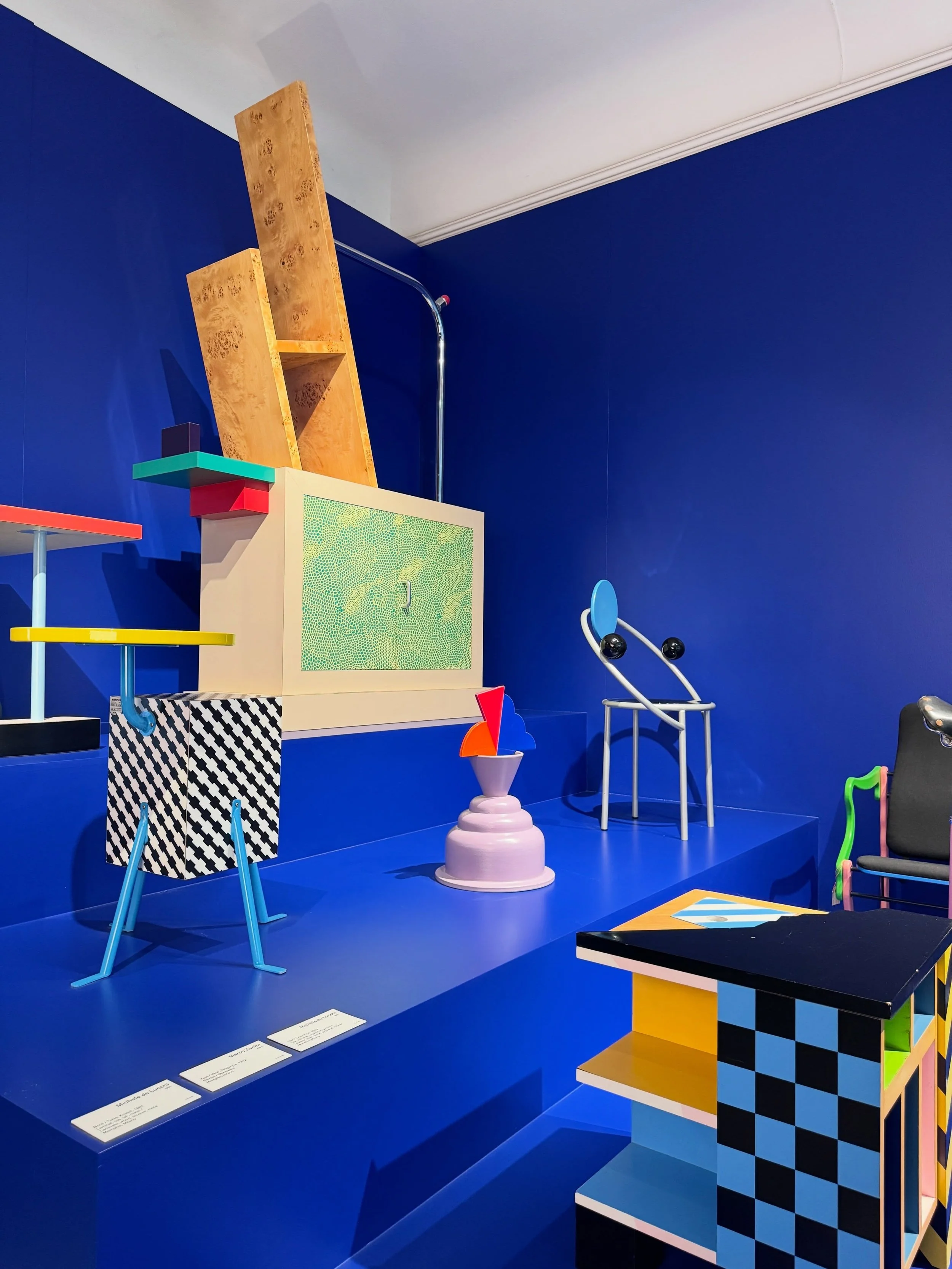 Colorful geometric objects and furniture in a blue-walled Designmuseum Danmark exhibition.