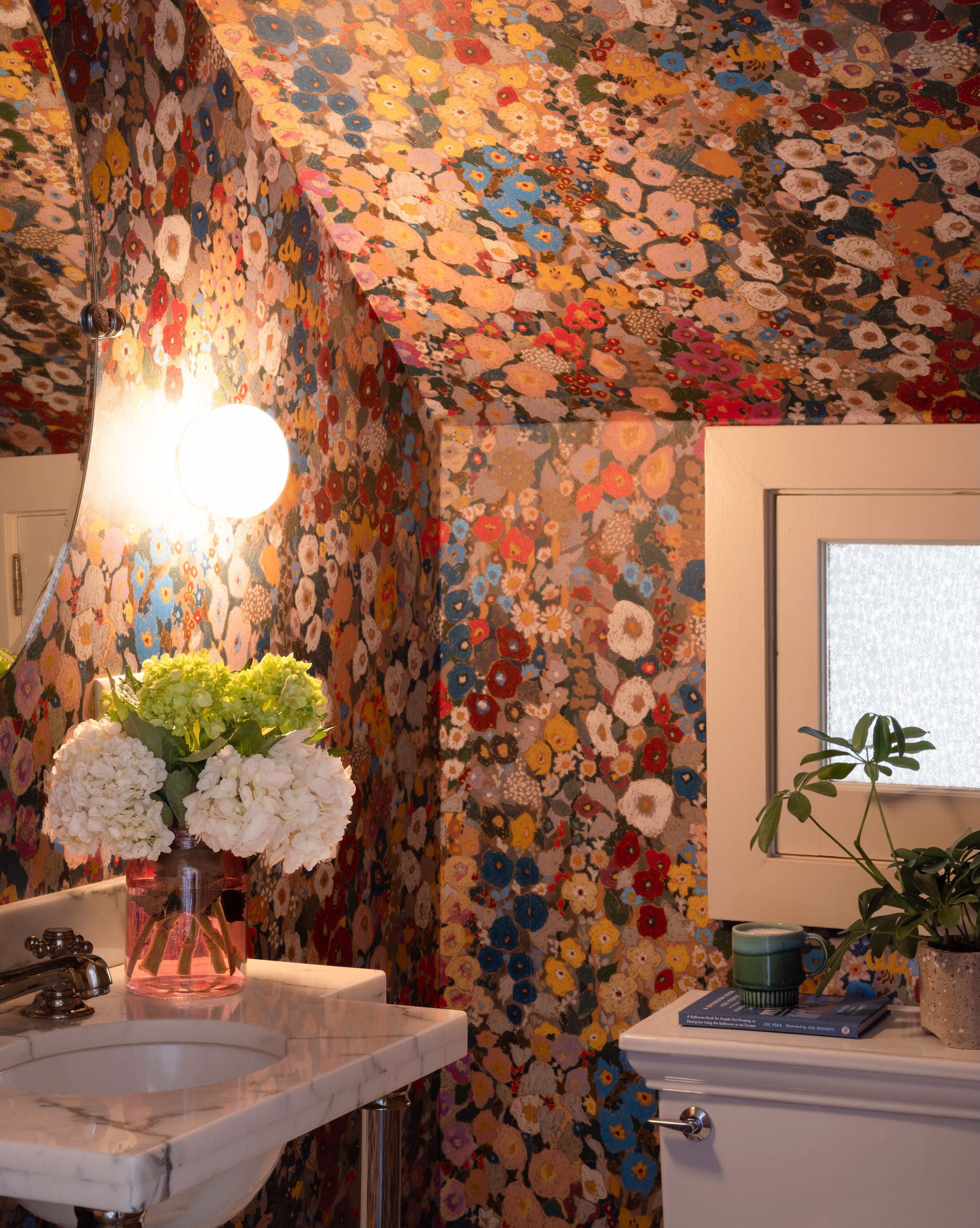 Powder-room detail with floral wallpaper, a wall light, mirror, and pale stone vanity.