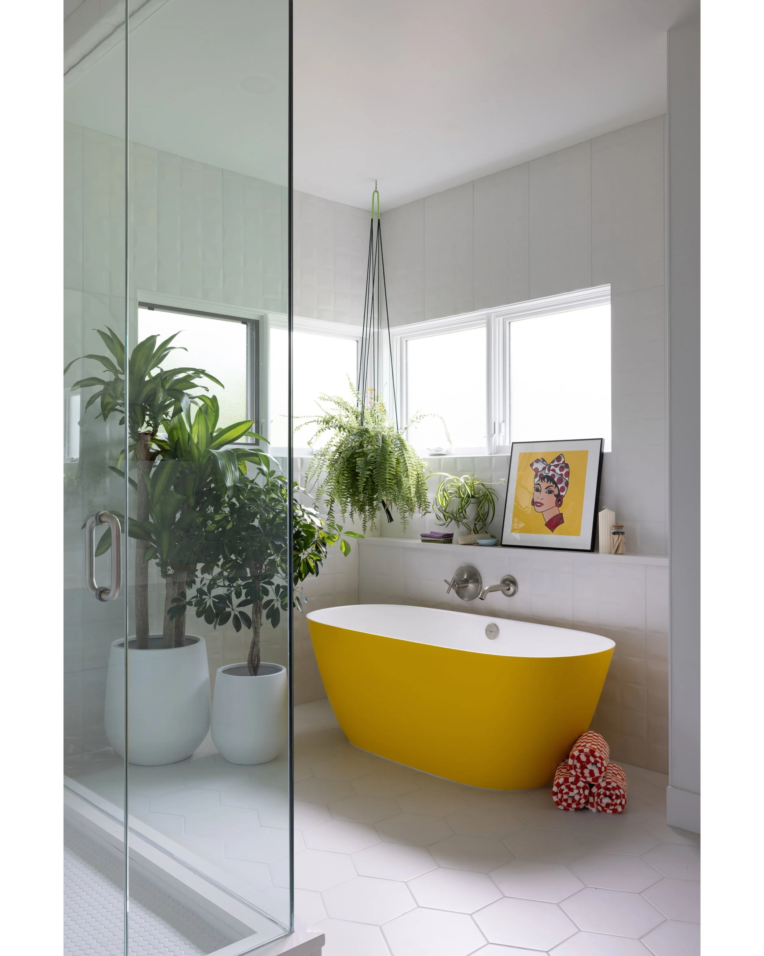 Bathroom with a yellow freestanding tub, white tile, a glass shower, and hanging plants.