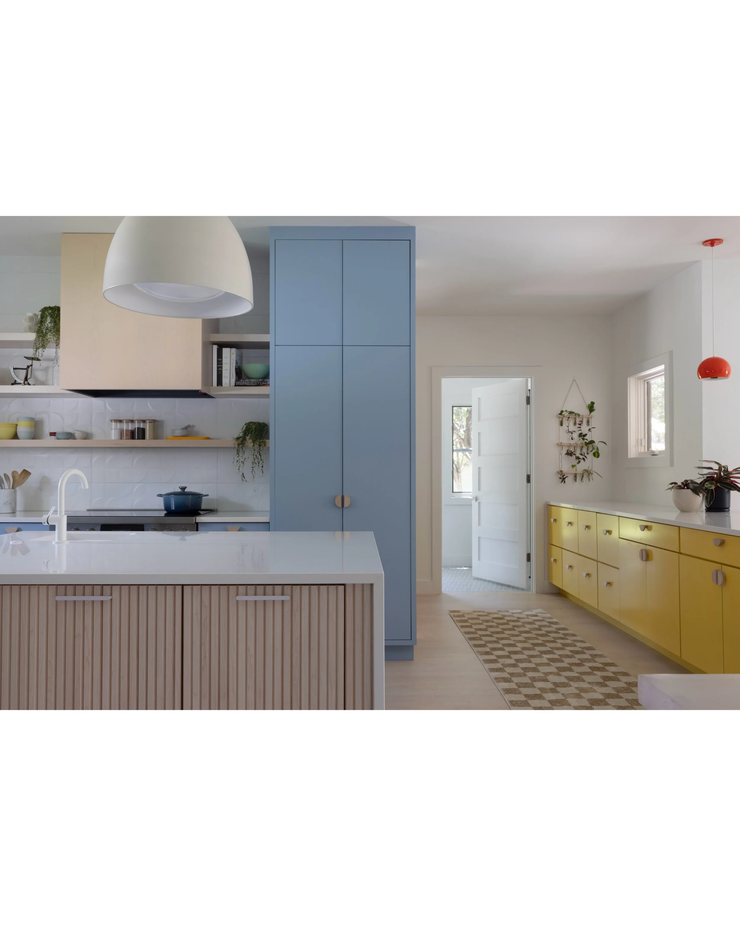Kitchen with pale blue pantry cabinets, yellow base cabinets, a fluted island, and white lighting.