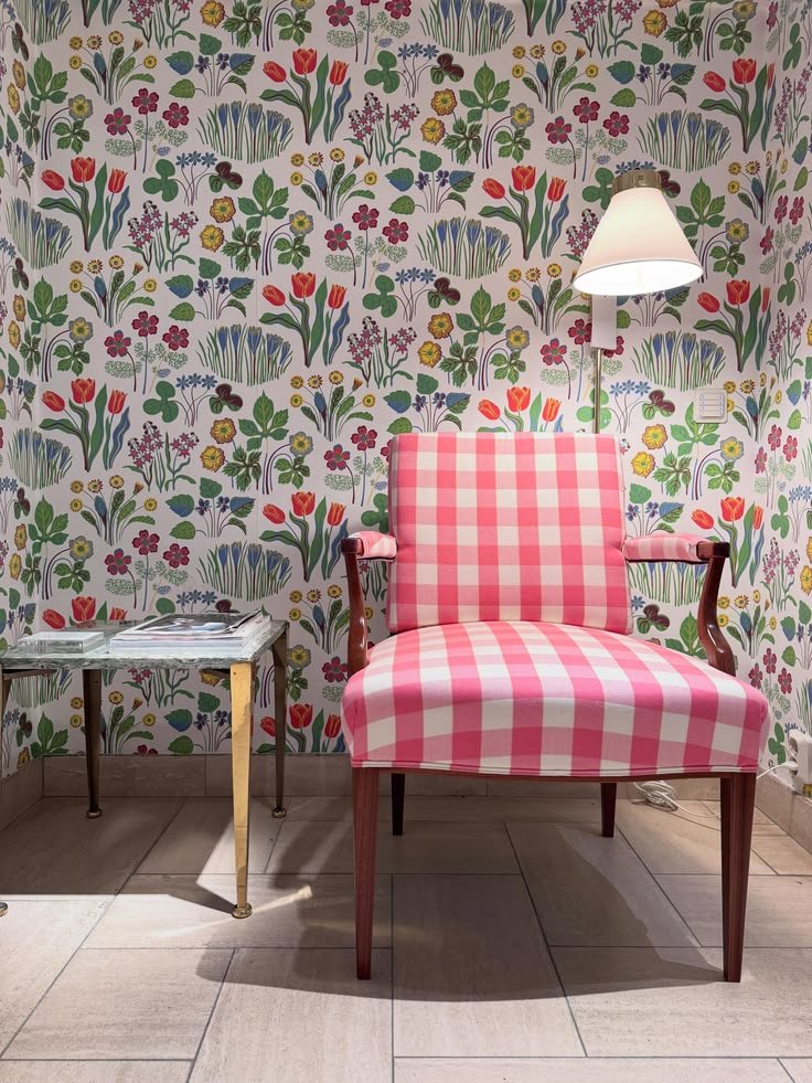 Pink gingham upholstered chair with a pleated white floor lamp and multicolored botanical wallpaper at Svenskt Tenn.