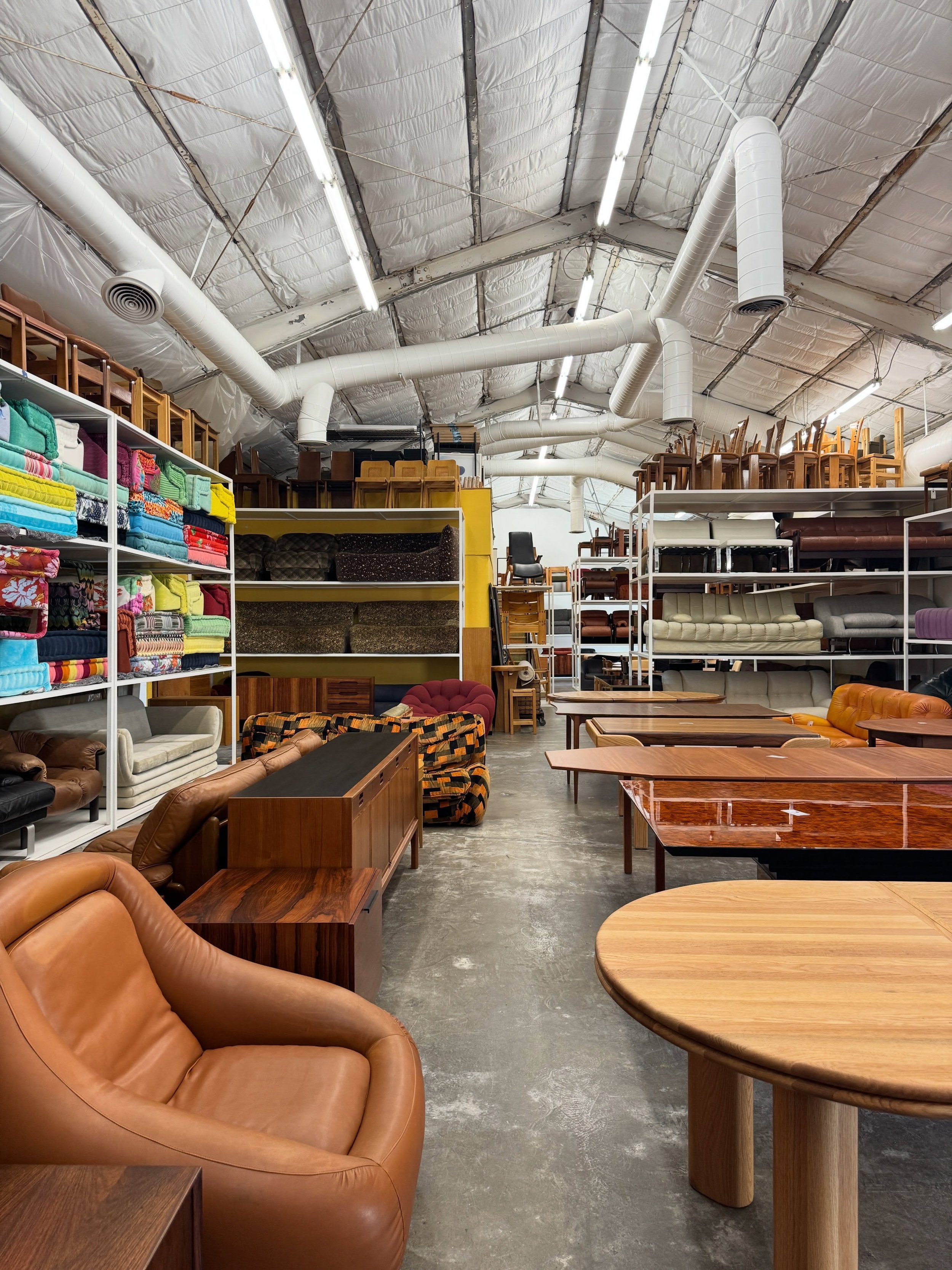 Mid Century LA showroom with leather seating, wood tables, vintage shelving, and exposed ceiling beams.