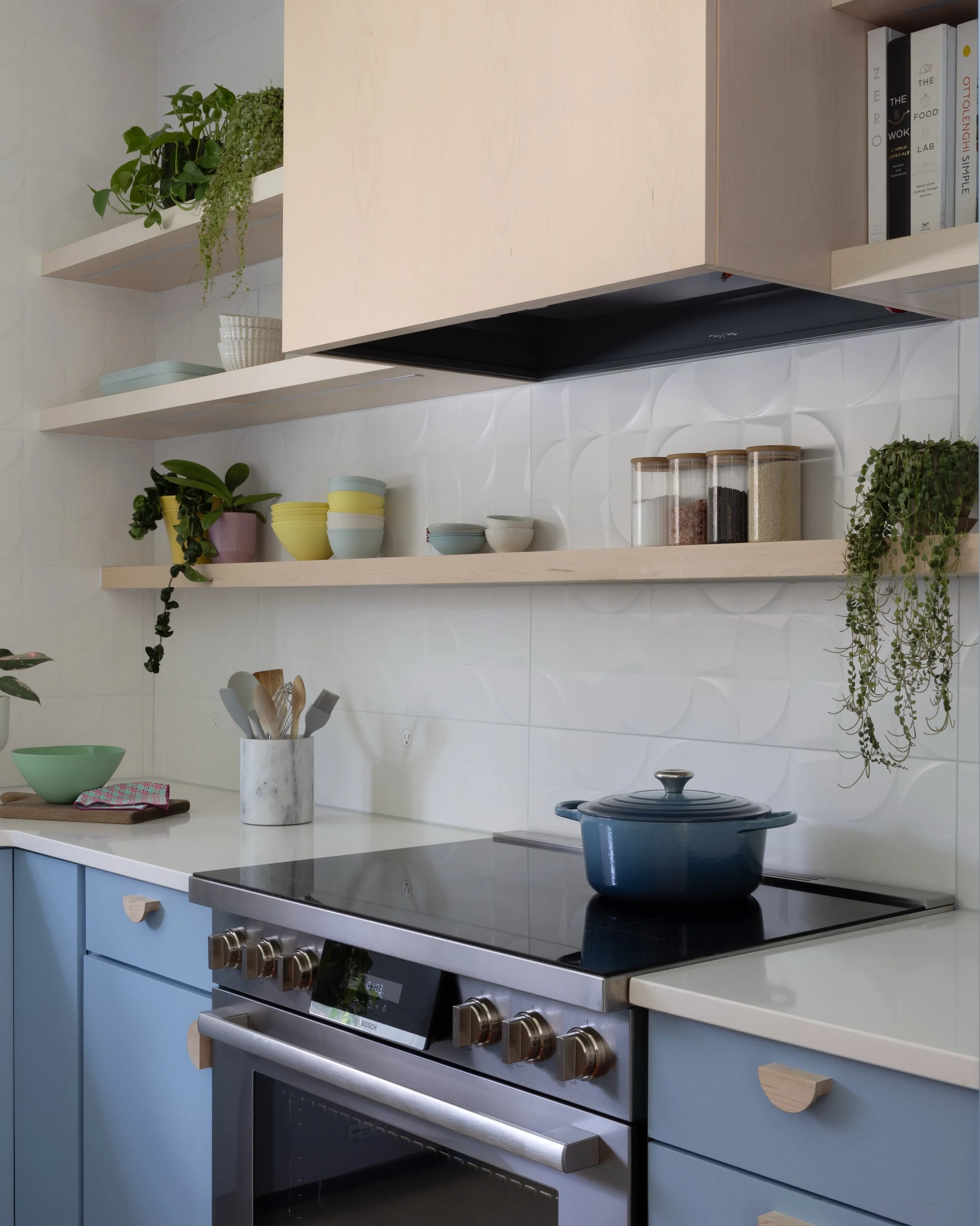 Kitchen with blue base cabinets, oak upper cabinets, a black range hood, open shelves, and pale countertops.
