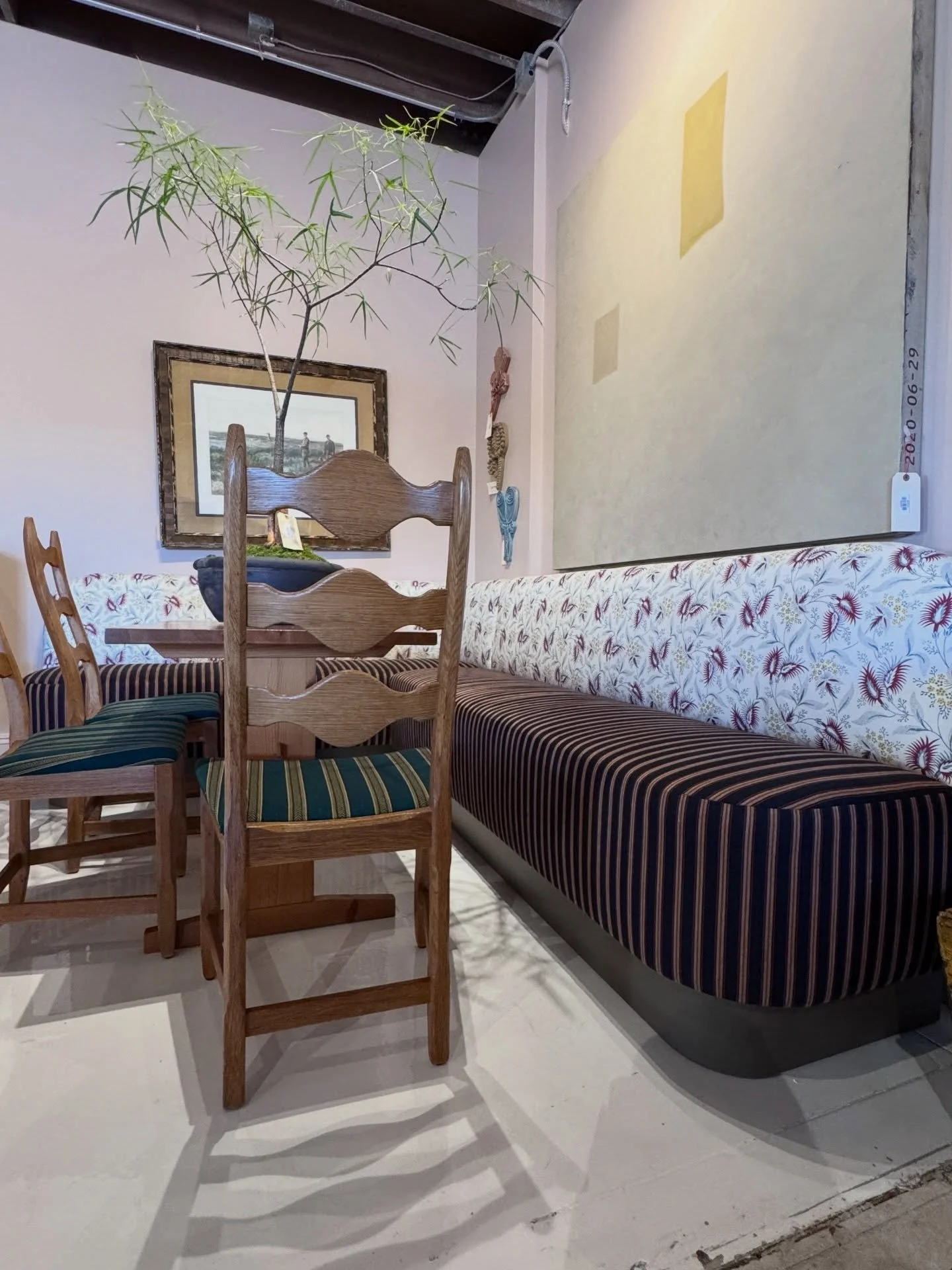 Vintage wood dining chairs beside a floral upholstered bench and framed art at Prairie Interiors.