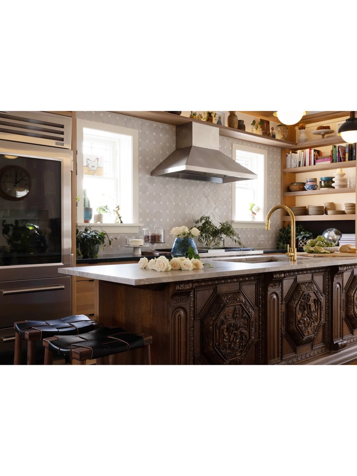 Kitchen with a carved wood island, stainless steel hood, pale backsplash, and open shelves.