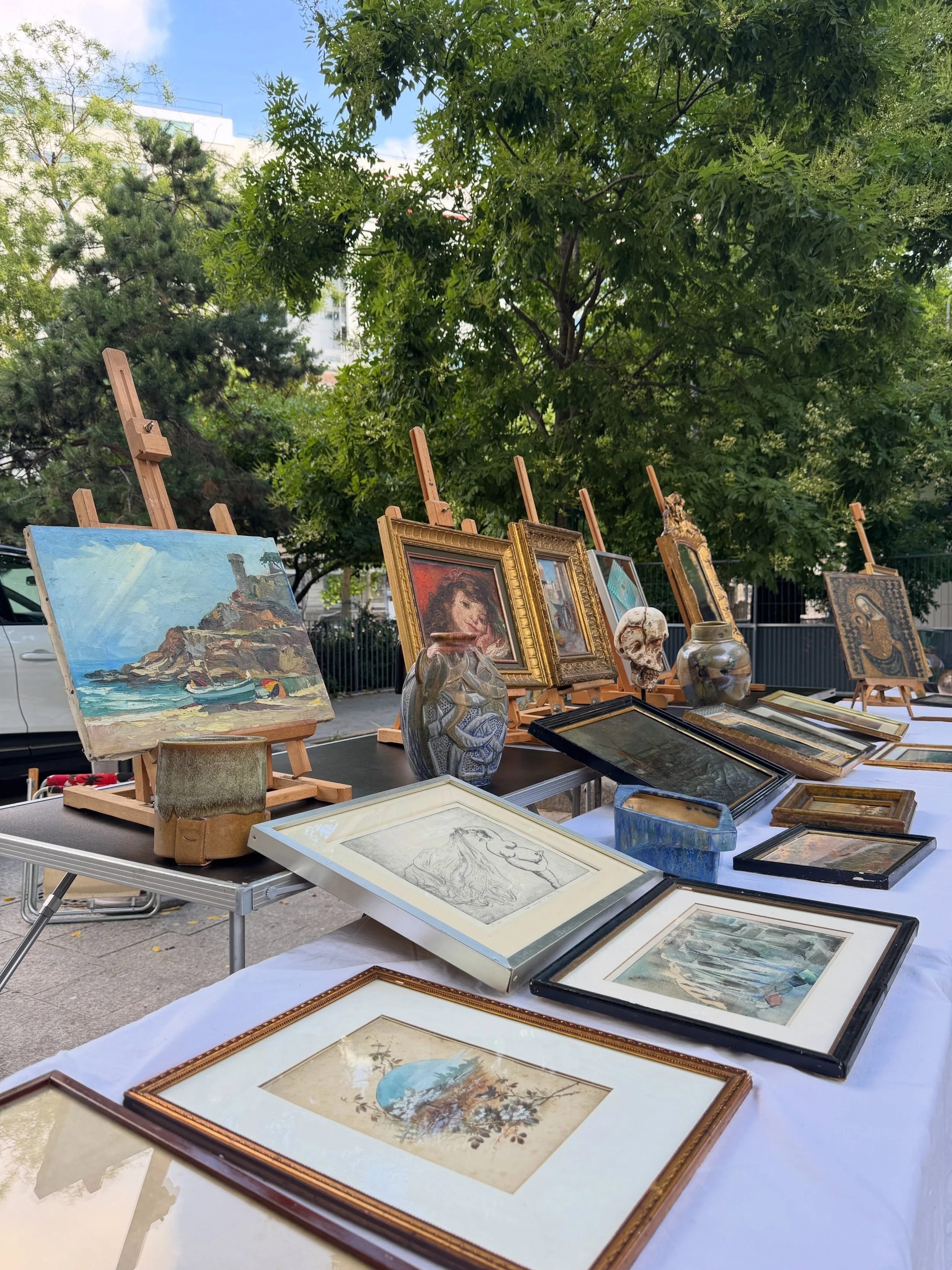 Framed paintings and vintage art arranged on a table at a Paris flea market.