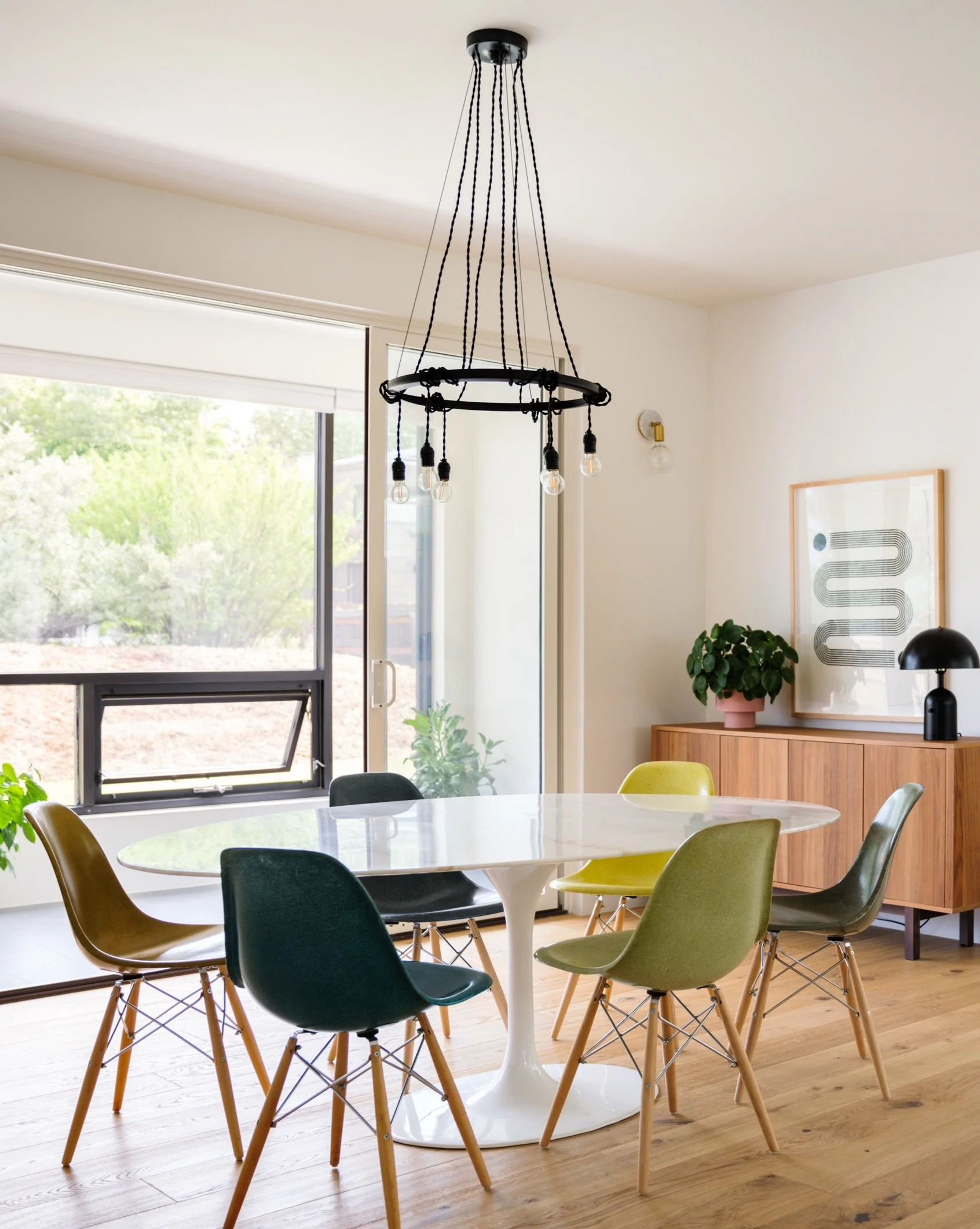 Boulder dining room with colorful shell chairs, wood table, black chandelier, and pale wood flooring.