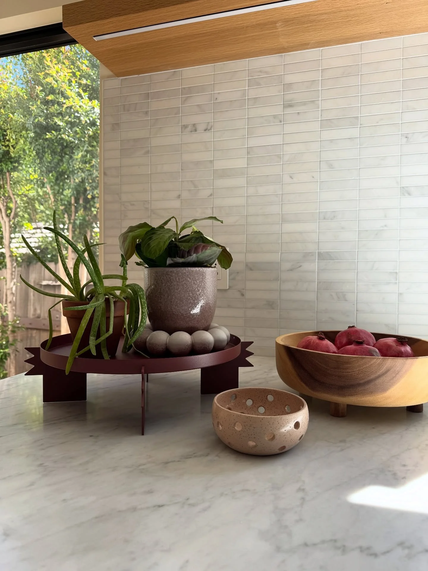 Upton sculptural burgundy plant stand with pottery and plants on a pale counter.