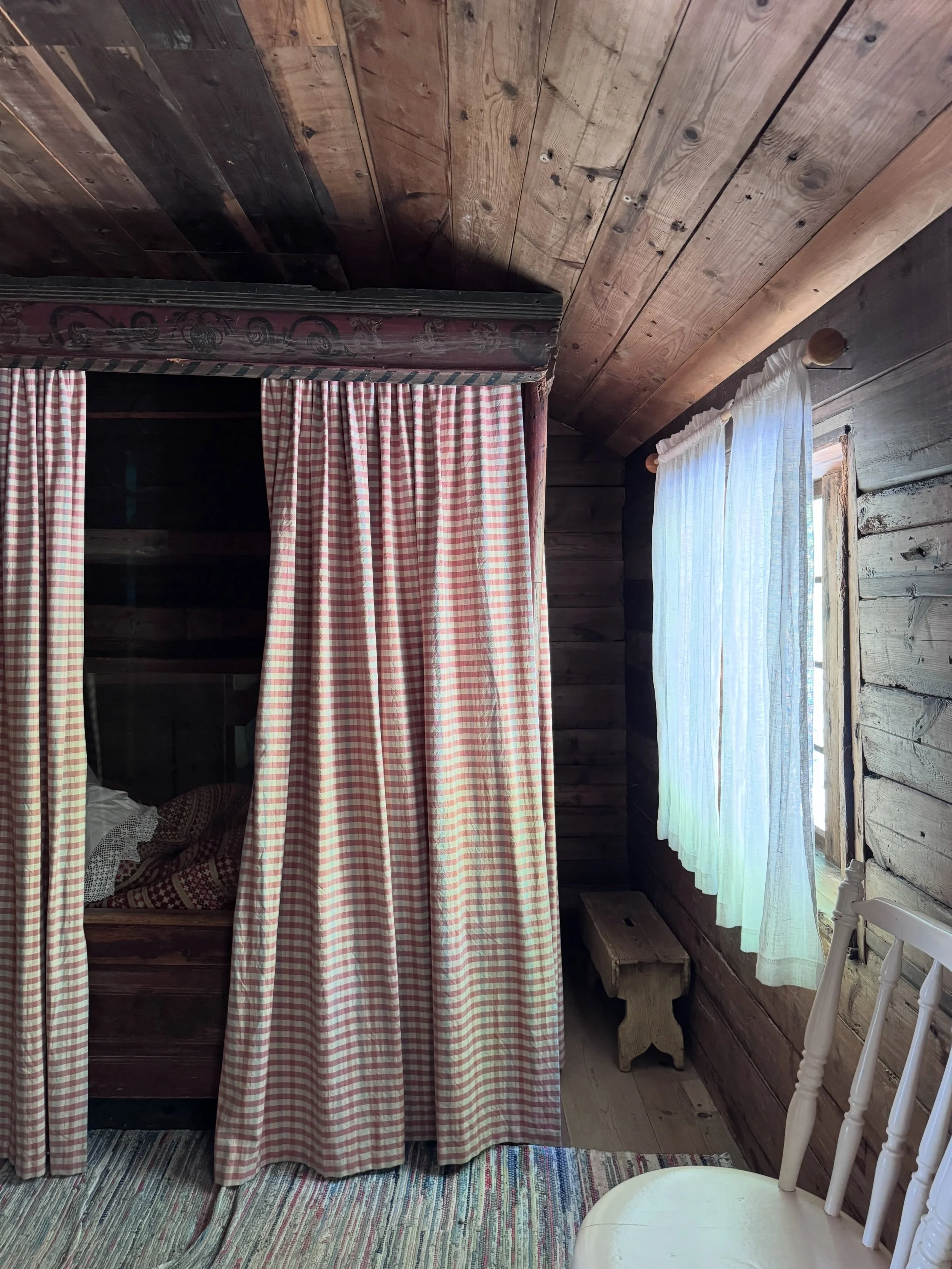 Norwegian cabin interior with a timber ceiling, red-and-white checked curtains, and white lace at the window.