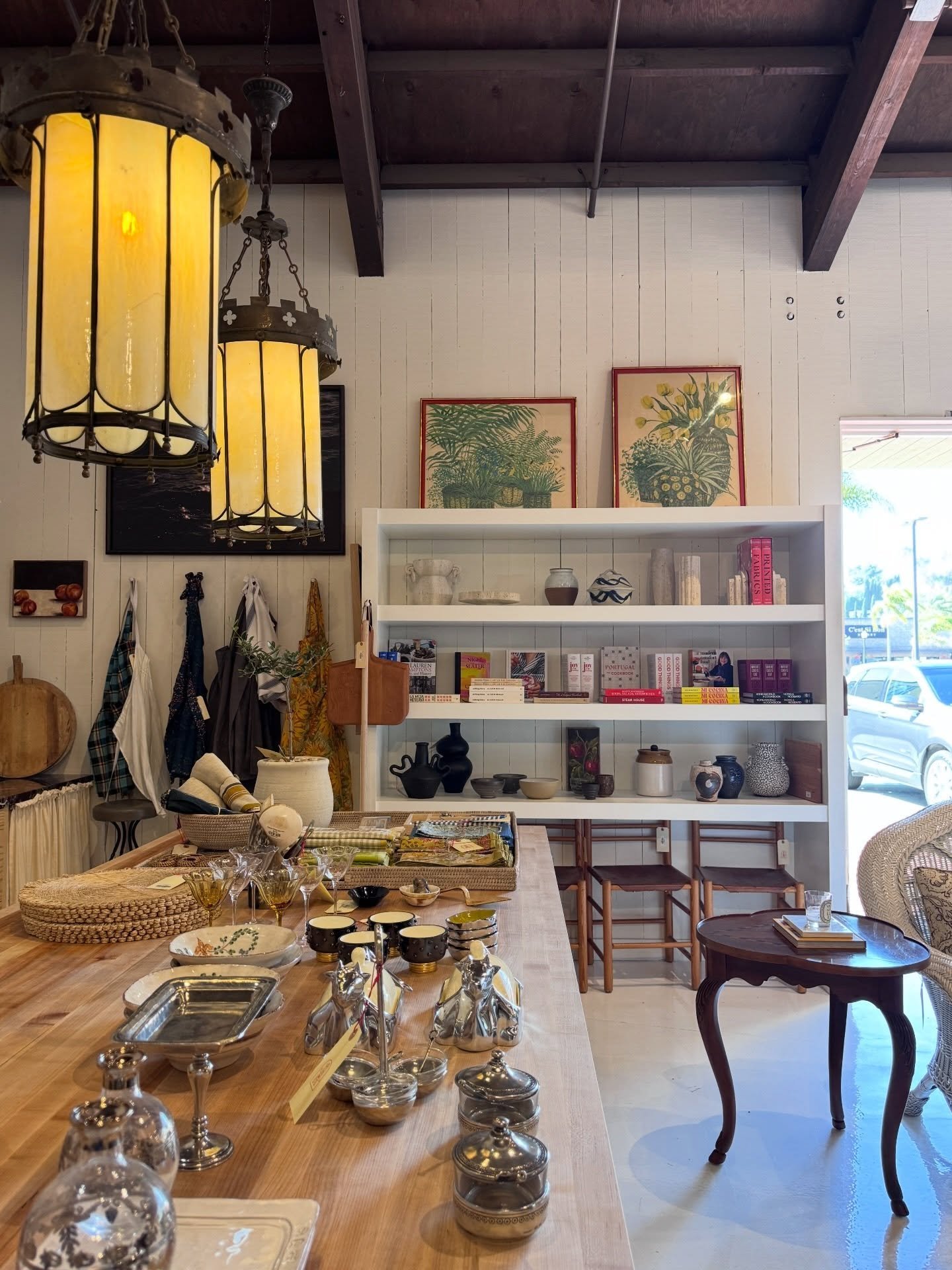 Vintage furniture, framed art, and decorative objects beneath yellow lanterns in a Newport Beach shop.