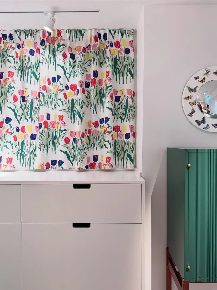 Multicolored floral curtain above white drawers beside a green radiator at Svenskt Tenn.