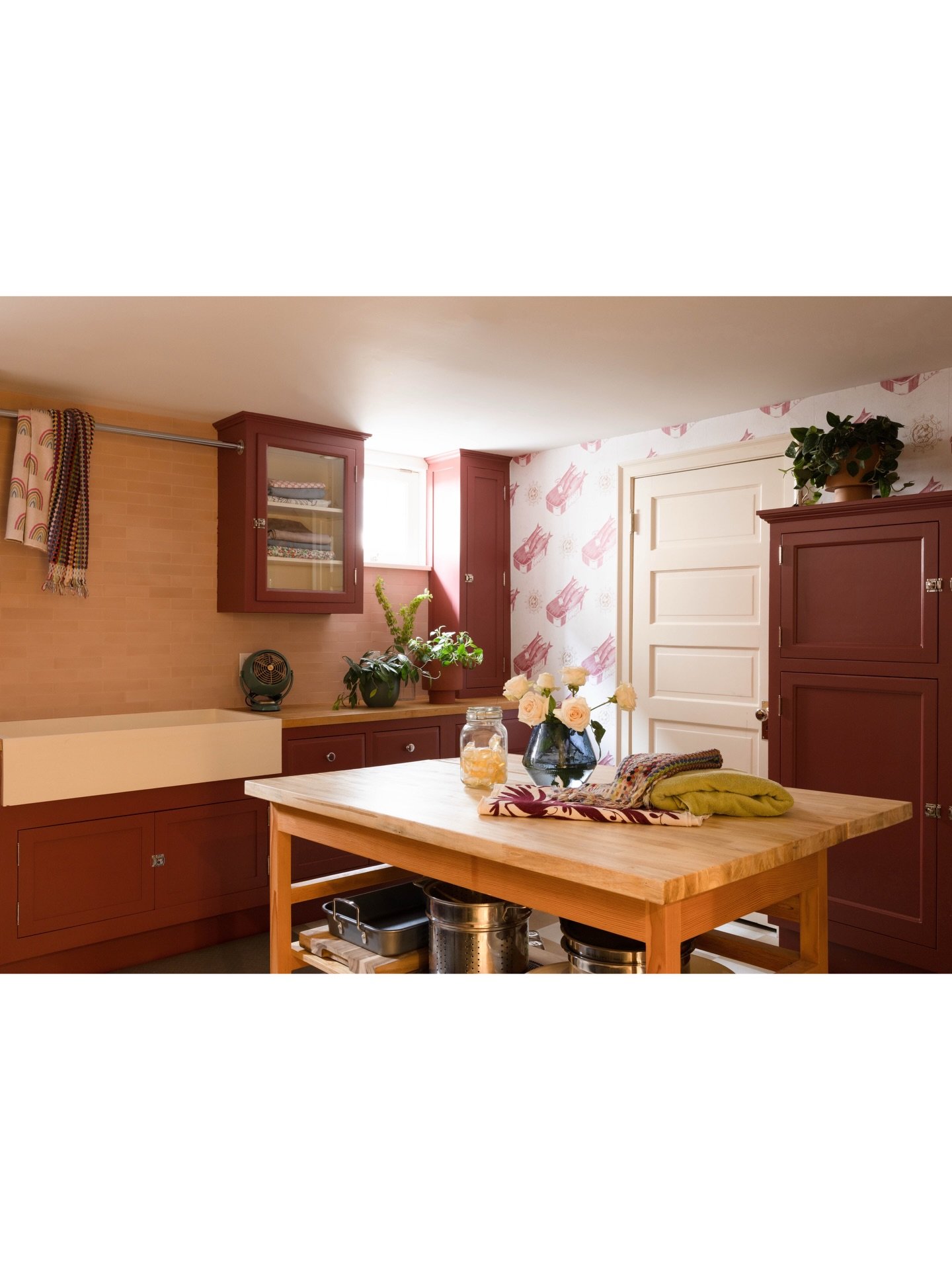 Kitchen and dining area with burgundy cabinets, a wood table, flowers, and pale walls.