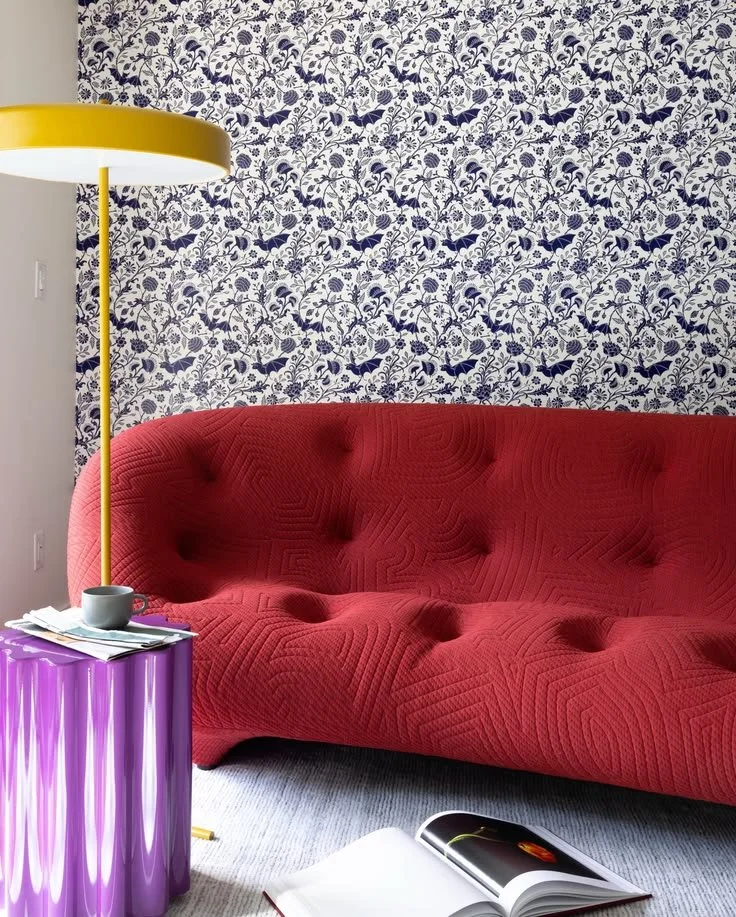 Red upholstered sofa with blue-and-white floral wallpaper, a purple side table, and yellow floor lamp.