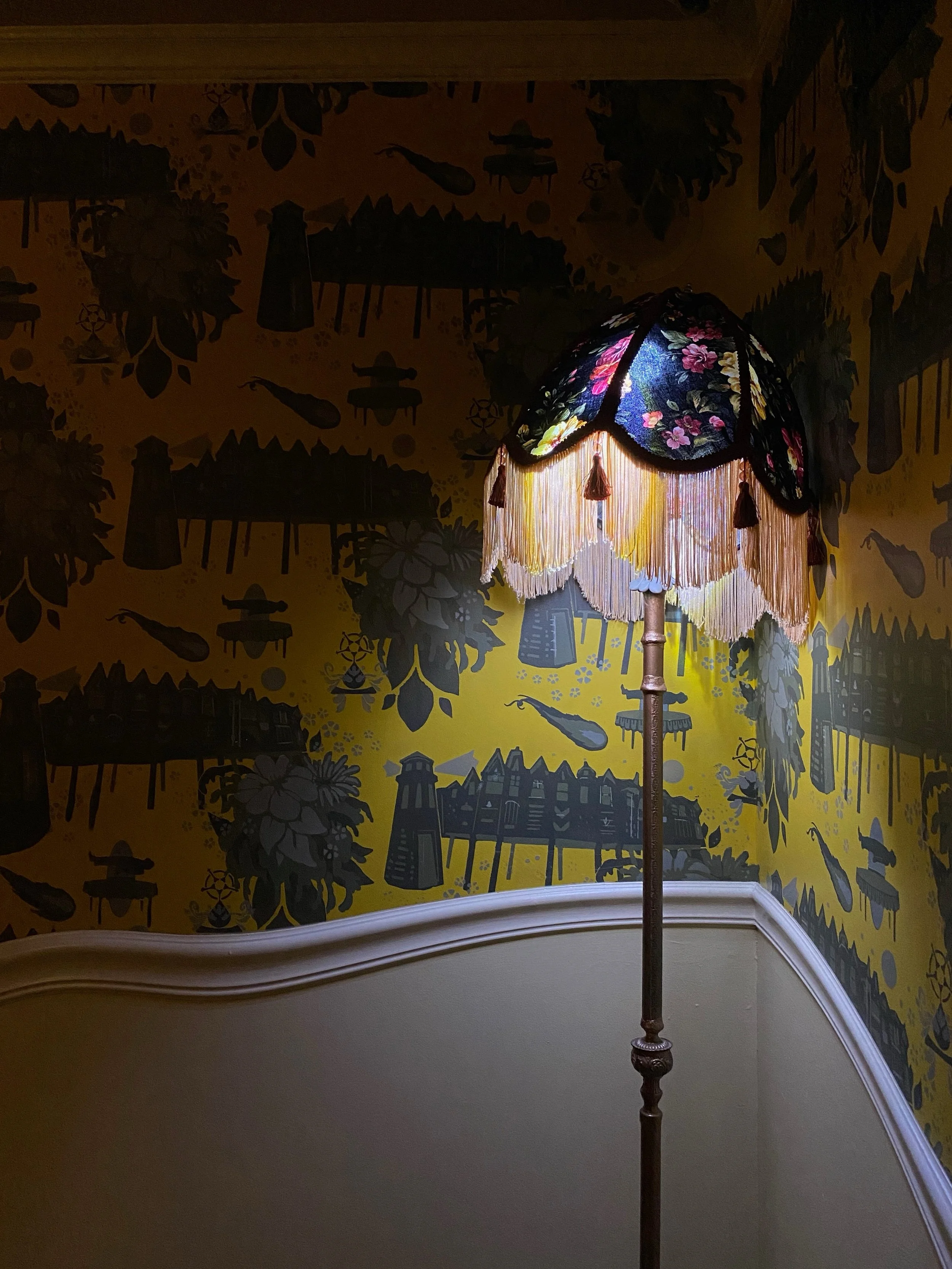 Glowing patterned lamp against yellow walls with dark silhouettes and curved stair trim at Meow Wolf Santa Fe.