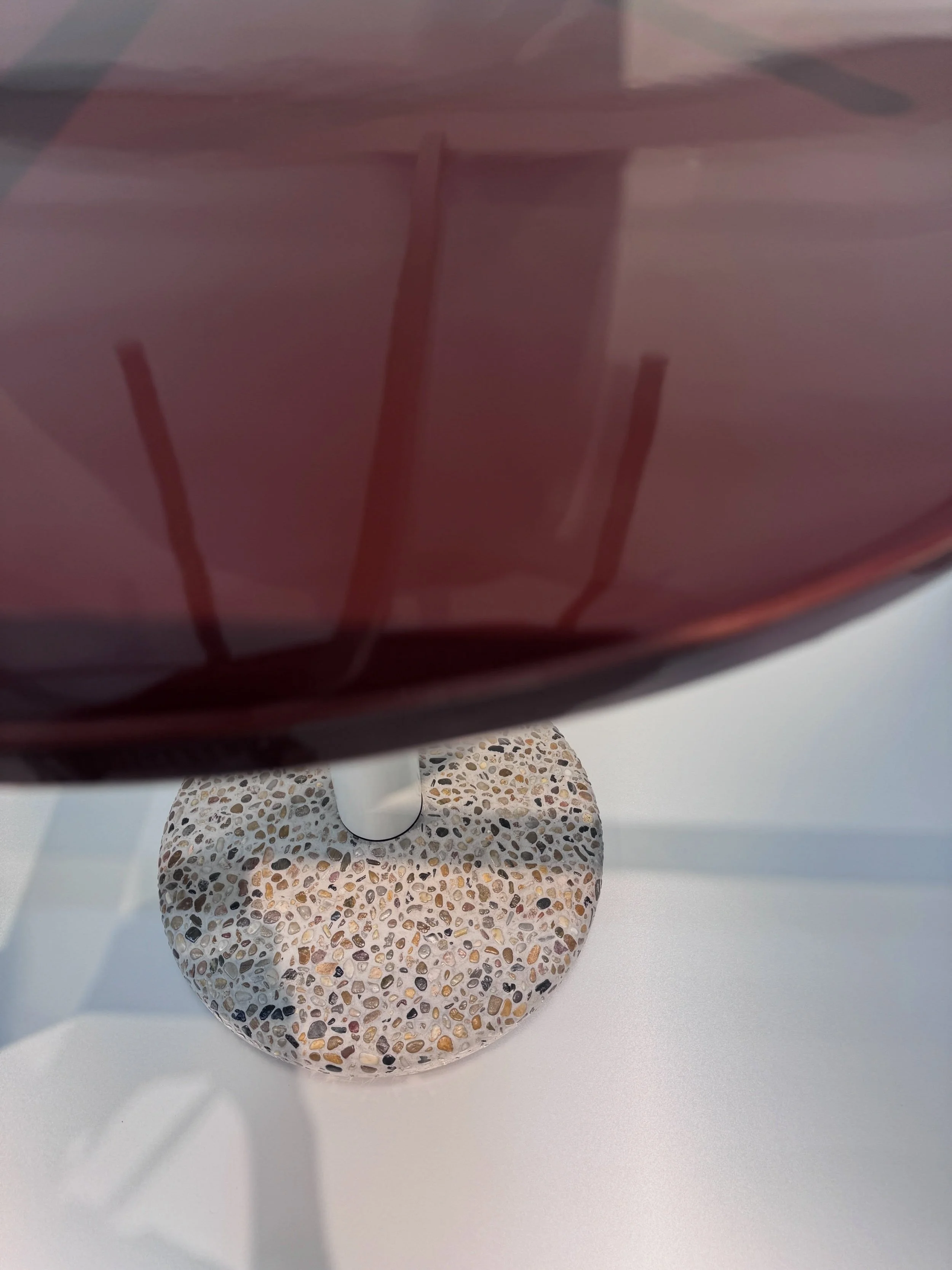 Detail of a red glass vessel above a speckled stone base.
