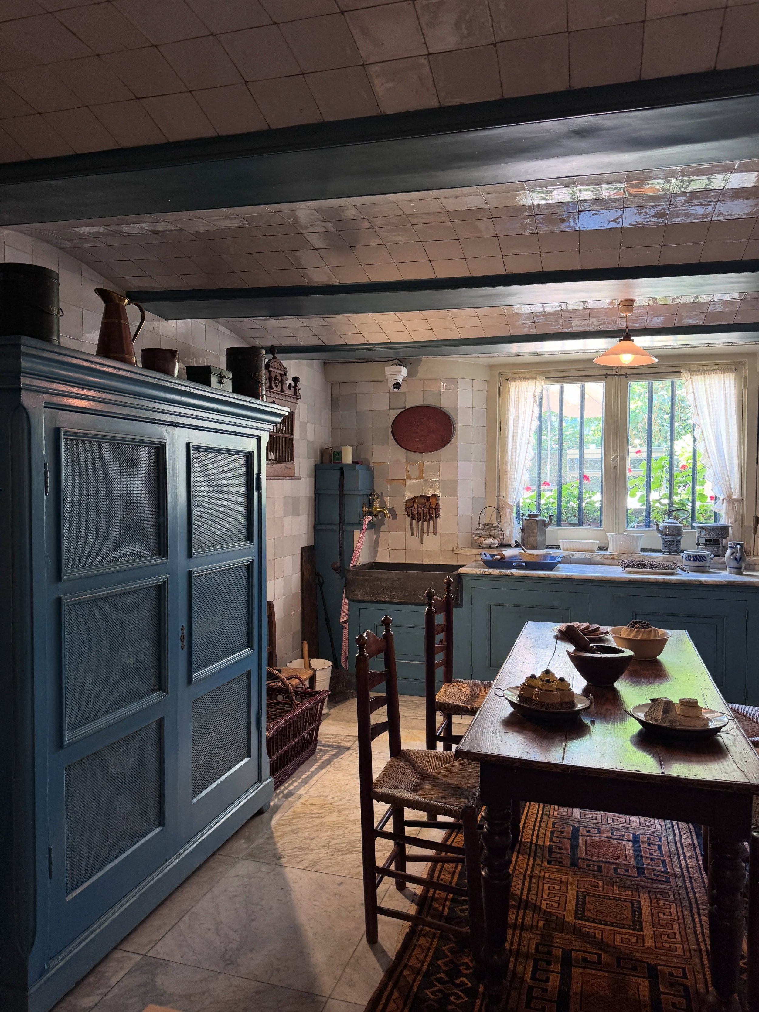 Historic Amsterdam interior with timber ceiling beams, a blue painted cabinet, wood table, and window seating.