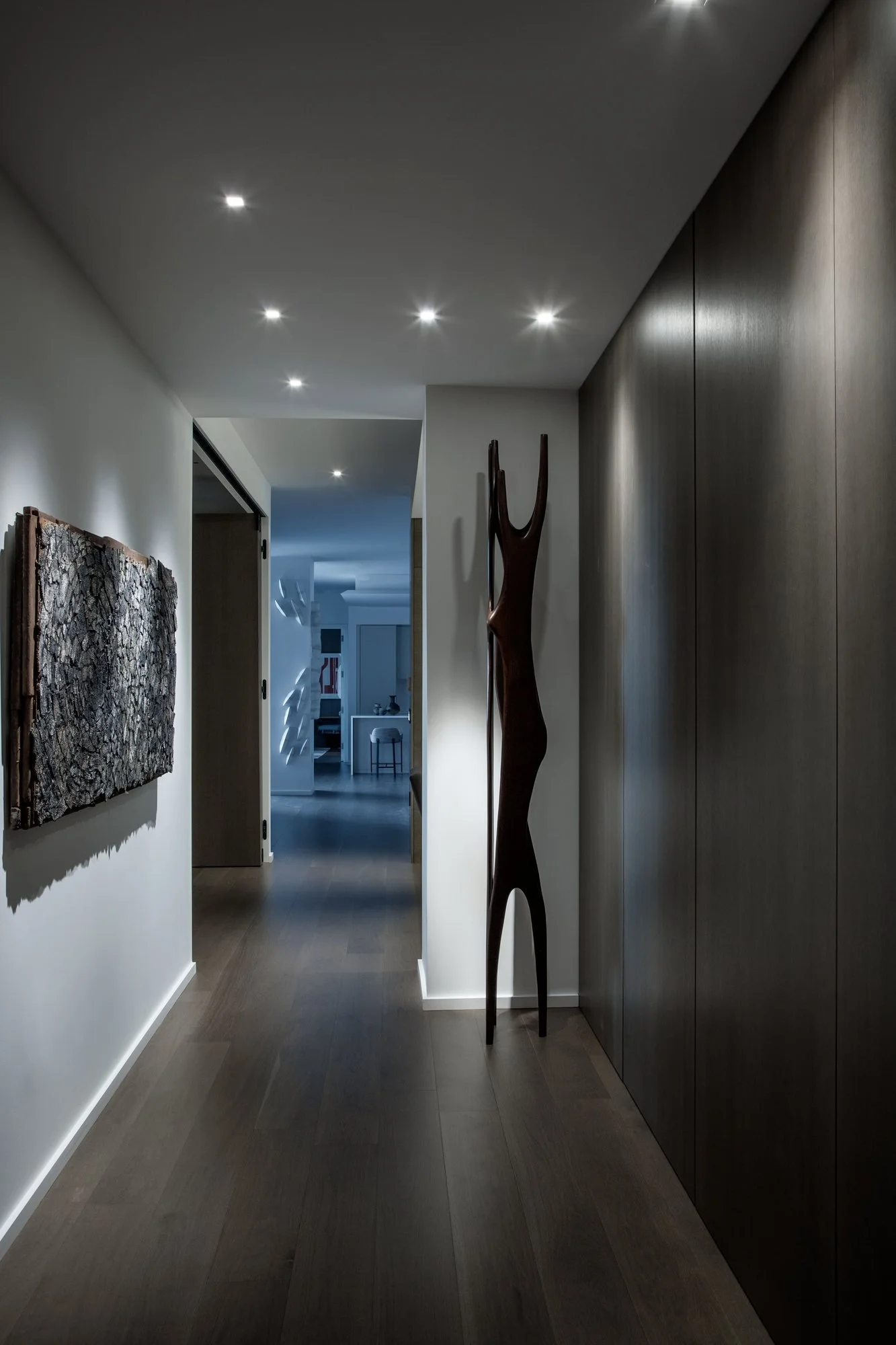 Long hallway with a full-height dark wood-panel wall, a carved wood sculpture and a textured wall piece