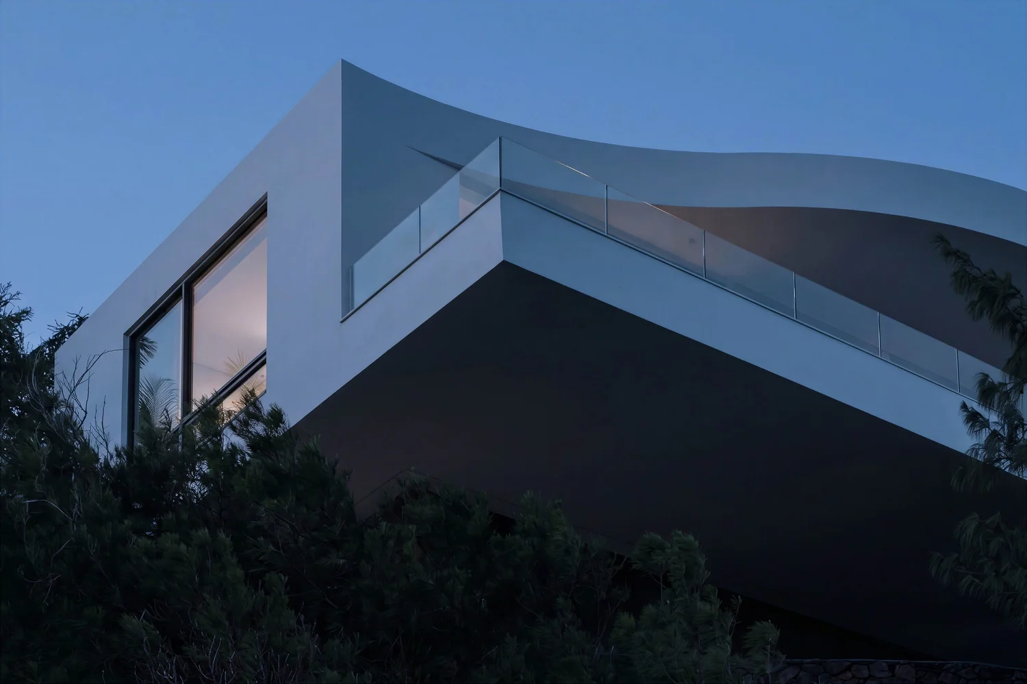 Cantilevered white house above ironwood trees at dusk, one window lit
