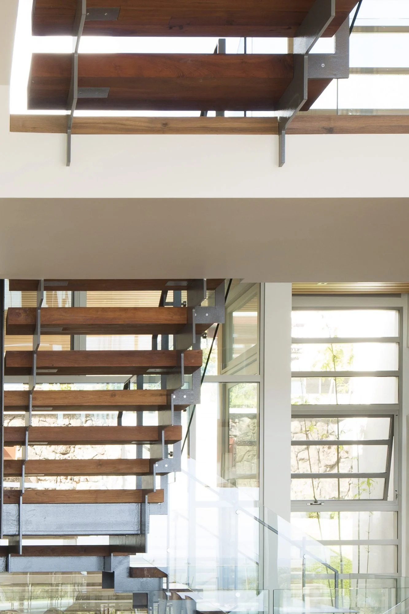 Open wood treads of the central stair on steel brackets, behind a glass rail