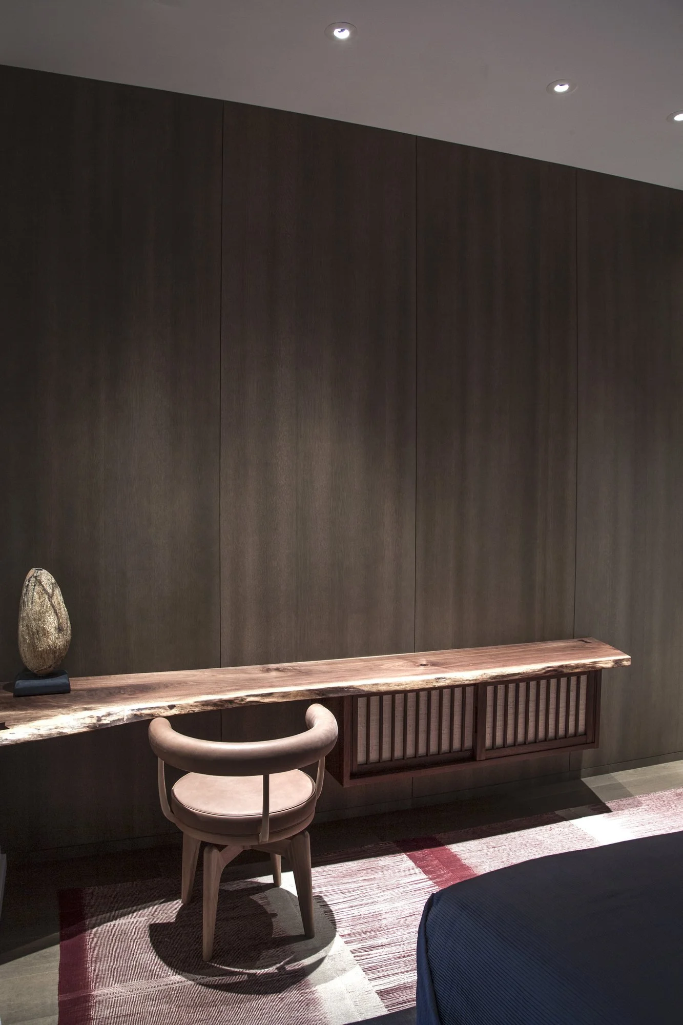 Live-edge wood desk floating against a wall of dark wood panels, with a round-backed chair