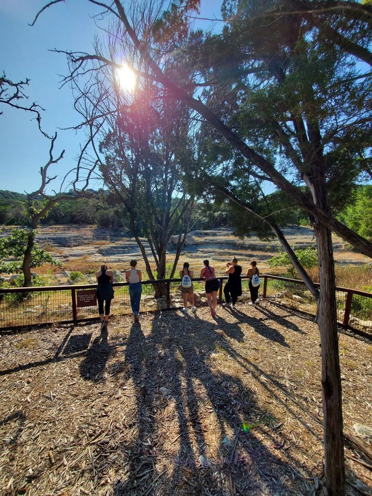 Walkers leaning on a railing at a Hill Country trail overlook, long shadows across the trail