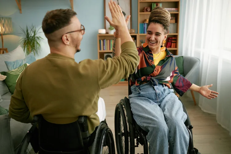 Two young adults in wheelchairs give a high five.