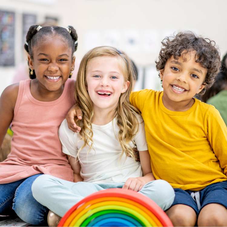 Three children smiling behind a wooden rainbow.