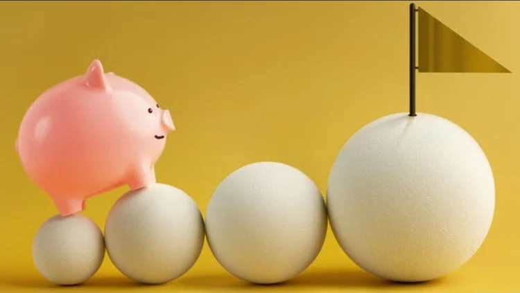 A pink piggybank is perched on top of white eggs of increasing size. The pig is facing a flag at the top of the largest egg,