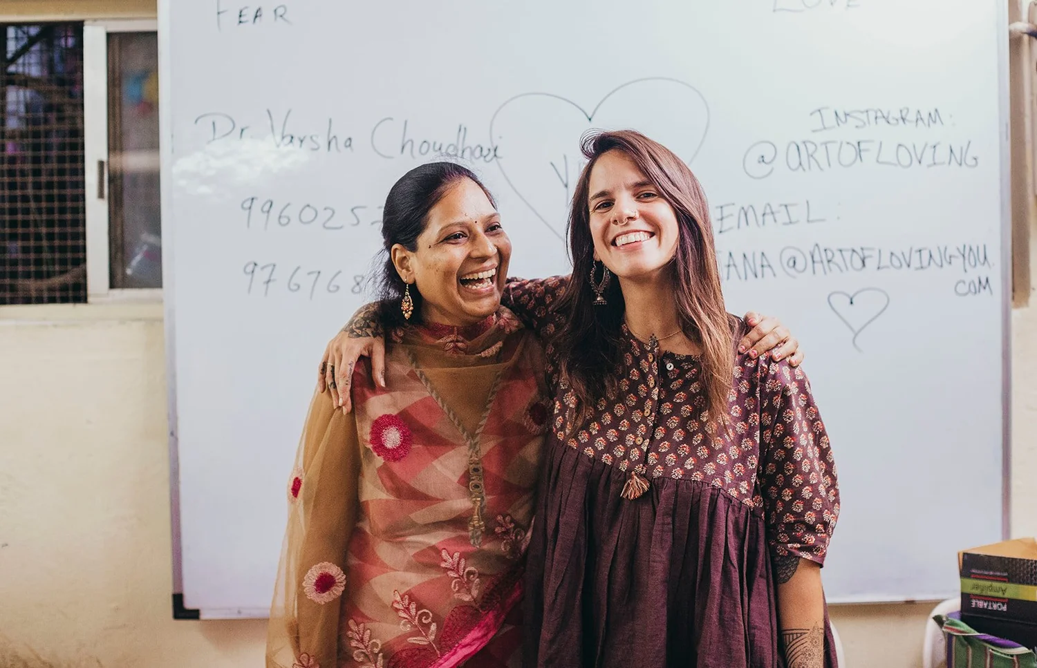 Dr. Varsha Choudhari and Adriana Rizzolo laughing with their arms around each other in a classroom in India